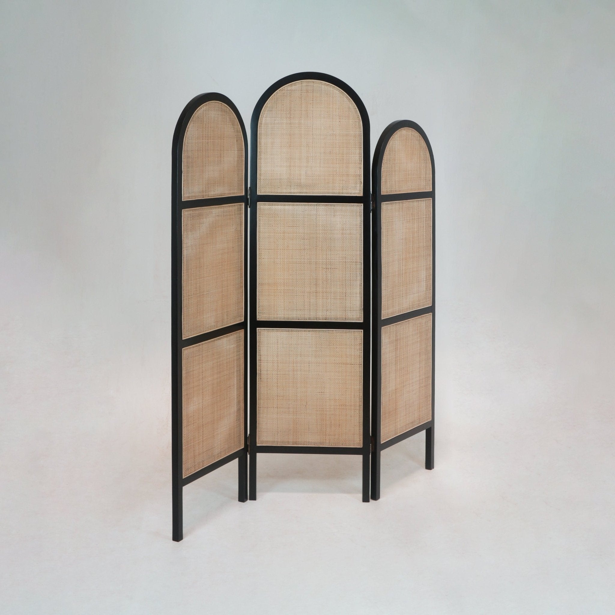Three-panel folding room divider with a black solid wood frame and natural rattan cane panels, featuring arched top panels and rectangular lower sections in a boho style.