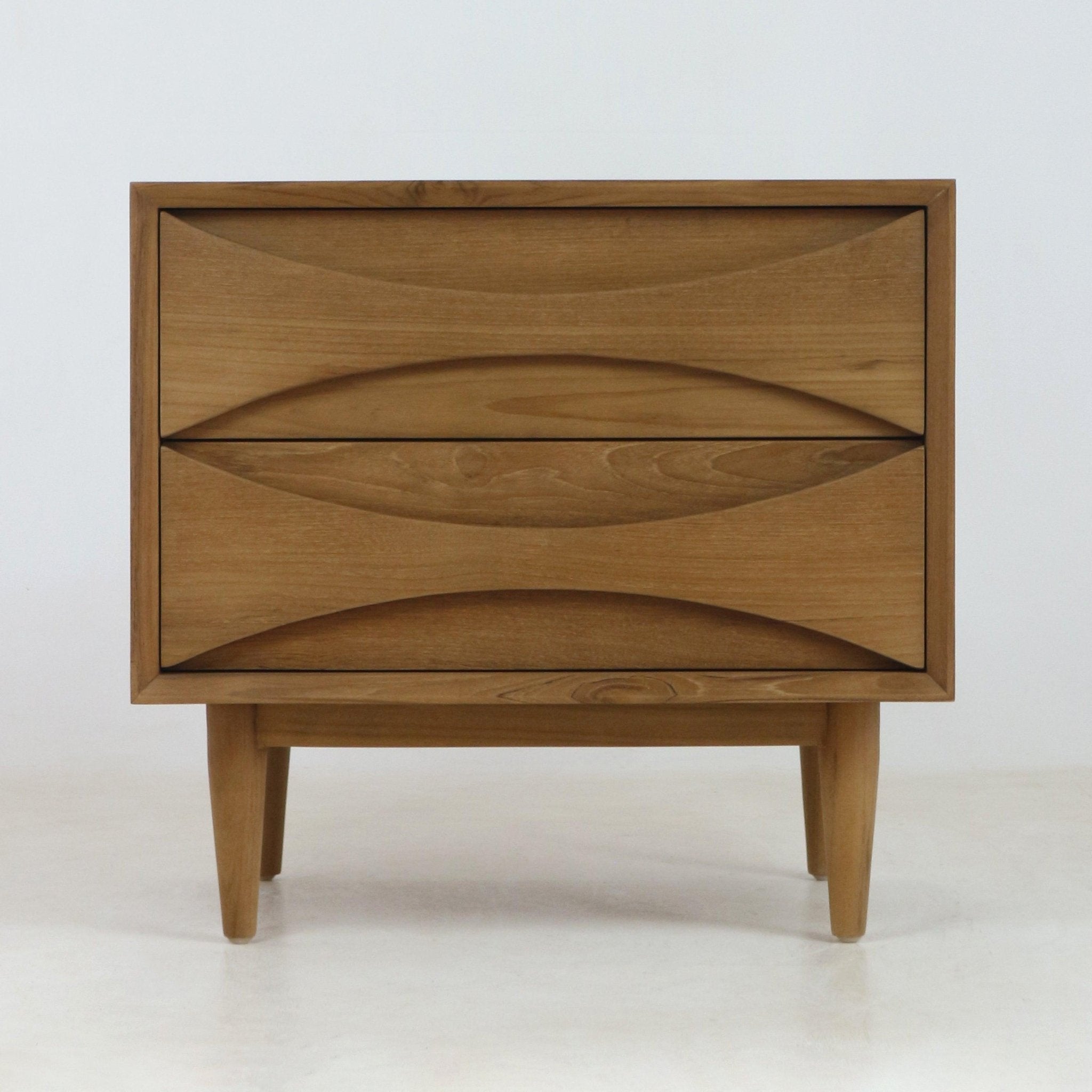 Natural teak two-drawer nightstand in mid-century Scandinavian style with carved recessed drawer pulls, tapered legs and warm wood grain finish shown on a pale neutral background.