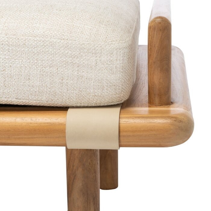 Close-up of a cream boucle bench cushion on a natural wood frame, showing the rounded corner, exposed leg and a beige leather strap securing the seat.