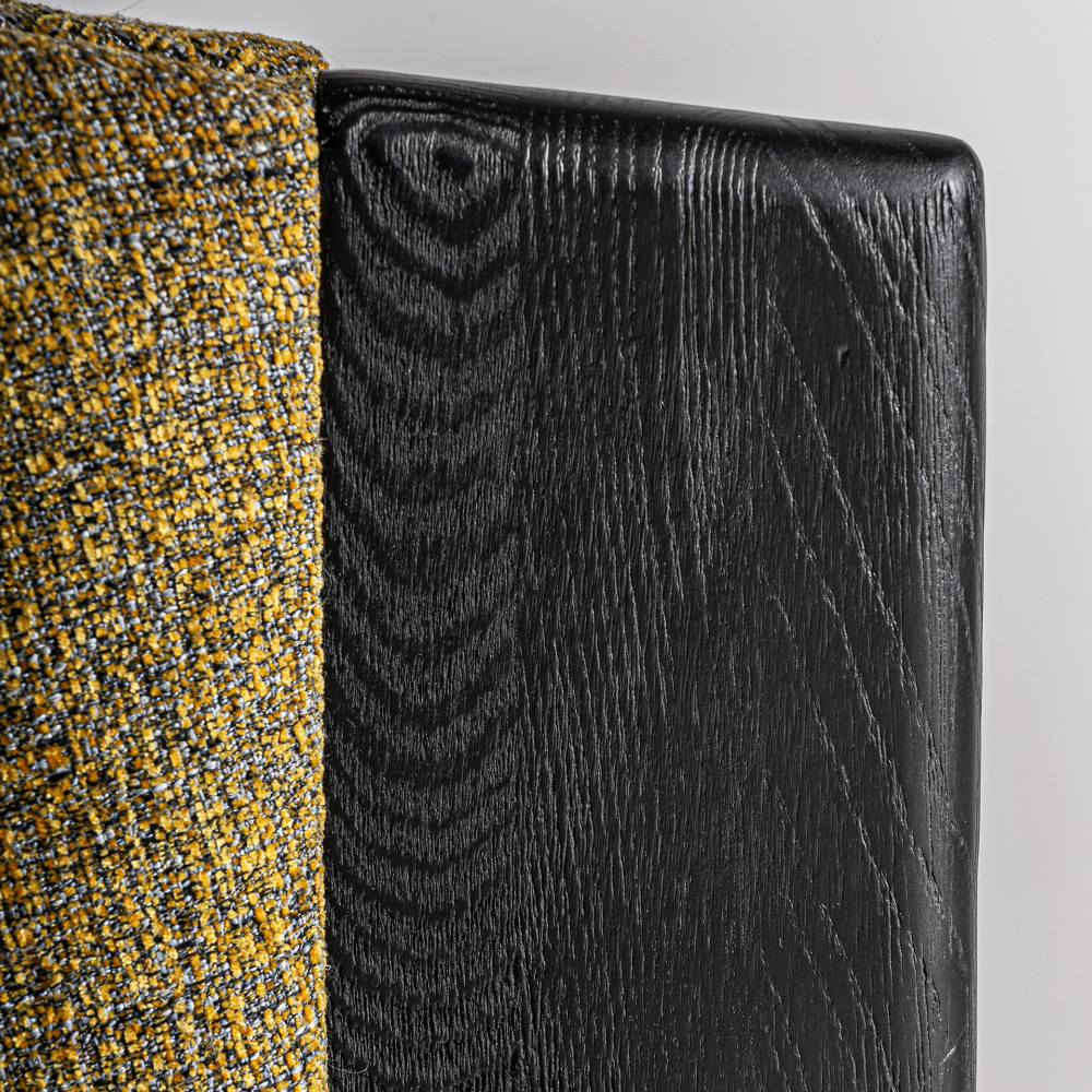 Close-up of a black-stained oak chair frame alongside mustard-yellow and gray woven performance fabric upholstery, highlighting the wood grain texture and the fabric's detailed weave.