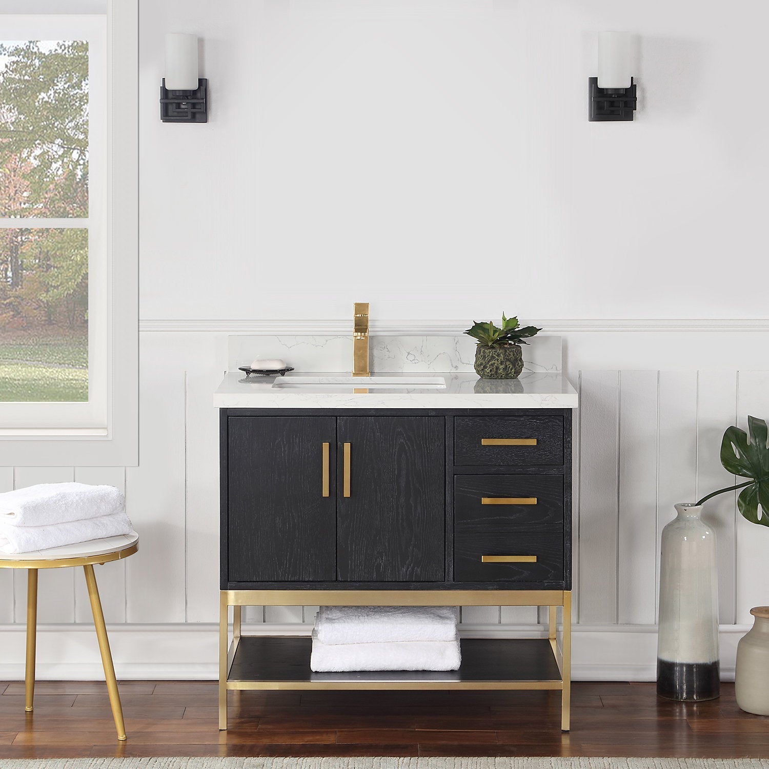 Modern 36-inch freestanding solid wood bathroom vanity in dark stained wood with white stone countertop, rectangular undermount sink, brass faucet and hardware, three drawers, cabinet doors and open lower shelf with towels.