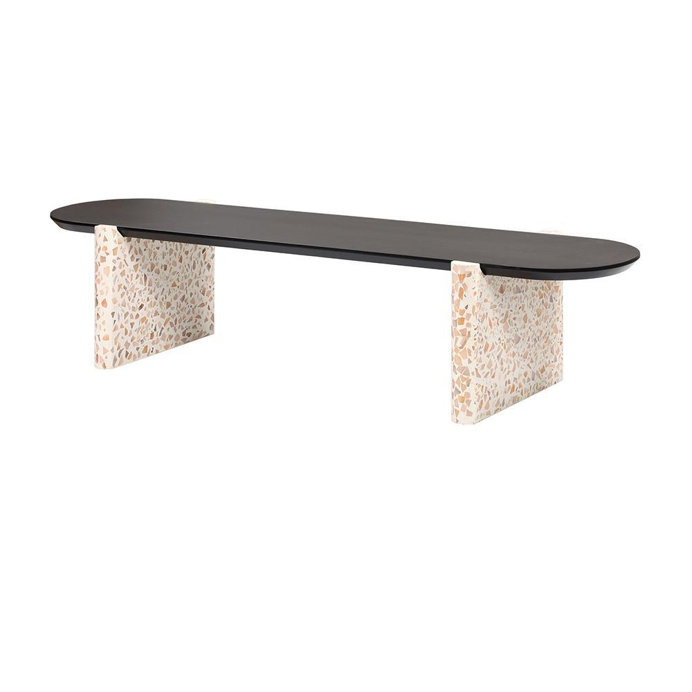 Minimalist modern coffee table with a long black oval wooden top resting on two cream terrazzo slab legs featuring beige and tan stone chips.