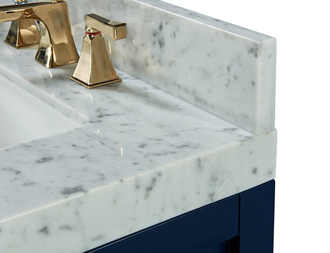 Close-up of white marble stone countertop and matching backsplash with gray veining, an undermount ceramic sink and brushed gold faucet set, mounted on a navy solid-wood vanity base.