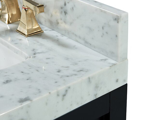 Close-up of a stone marble countertop with gray veining and matching backsplash, an integrated ceramic sink, polished brass faucet, and the edge of a black solid-wood vanity base.