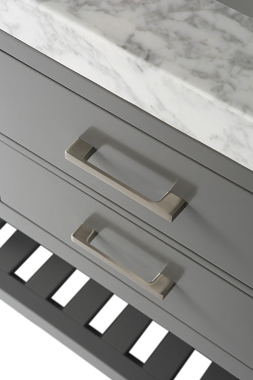 Close-up of a stone marble countertop resting on a stone-gray solid wood vanity with two brushed-gold rectangular drawer pulls and a slatted lower shelf visible beneath the drawers.