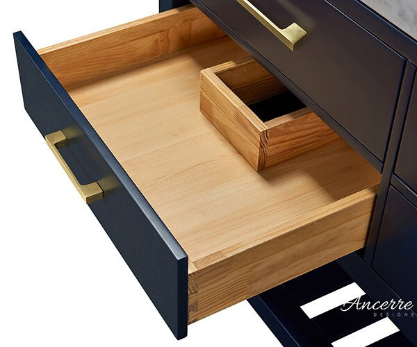 Close-up of an open vanity drawer showing a solid wood interior with a rectangular plumbing cutout, paired with a dark stone-finish drawer front and brushed gold rectangular handle.