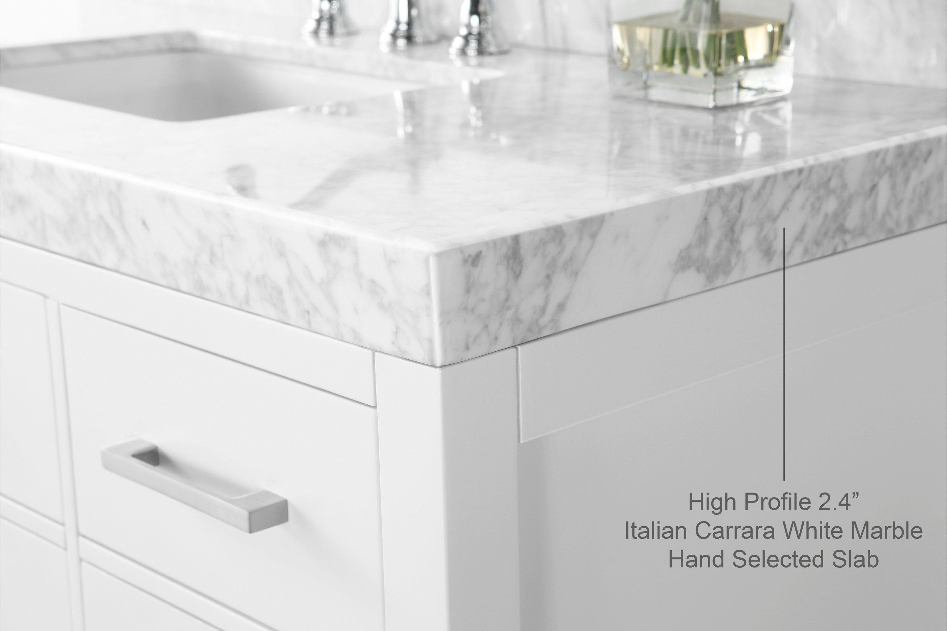 Close-up of a high-profile Carrara white marble countertop corner on a white solid wood bathroom vanity with a brushed metal drawer pull and subtle reflections of chrome faucet hardware.