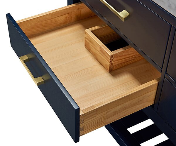 Open solid-wood vanity drawer showing a smooth natural wood interior with a small partitioned box for plumbing, set in a stone-colored contemporary vanity with a dark exterior and brass bar handle.
