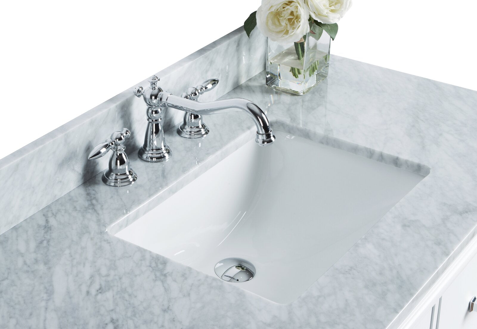 Close-up of a stone countertop with a white ceramic undermount sink, polished chrome widespread faucet and handles, and a small glass vase of white roses on the back ledge.
