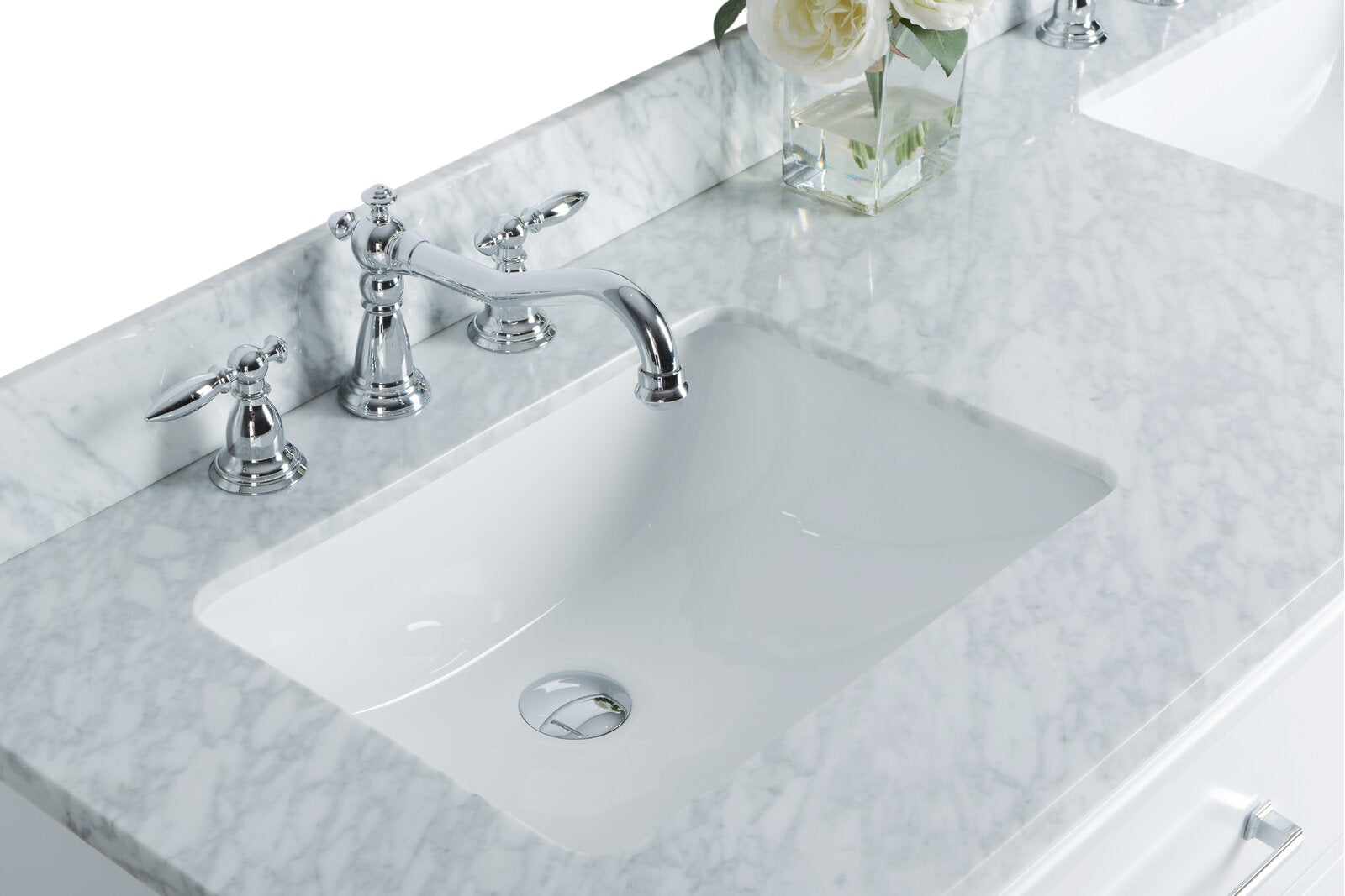Close-up of a stone marble countertop with an undermount white ceramic sink, polished chrome widespread faucet and lever handles, a clear square vase with white roses, and a glimpse of the white vanity drawer.