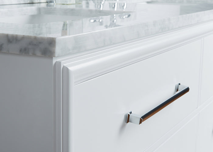 Close-up of a modern white solid-wood bathroom vanity drawer featuring a chrome bar pull and the light stone marble-look countertop edge with part of the double-sink surface and faucet reflection.