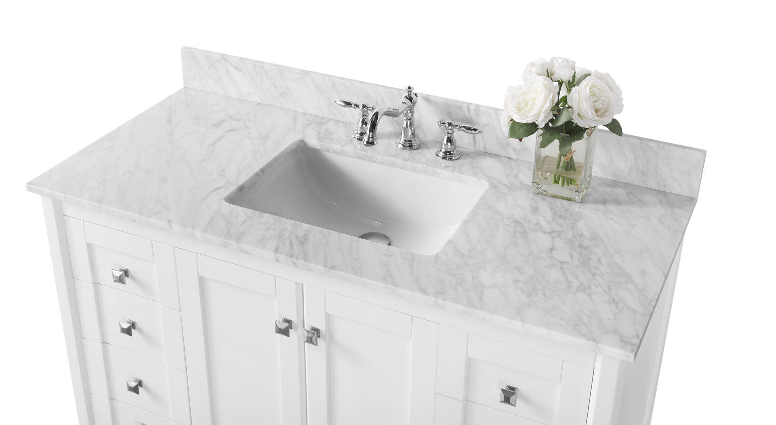 White solid wood bathroom vanity with a stone marble countertop, rectangular undermount ceramic sink, chrome widespread faucet, square chrome knobs, and a glass vase of white roses on the right.