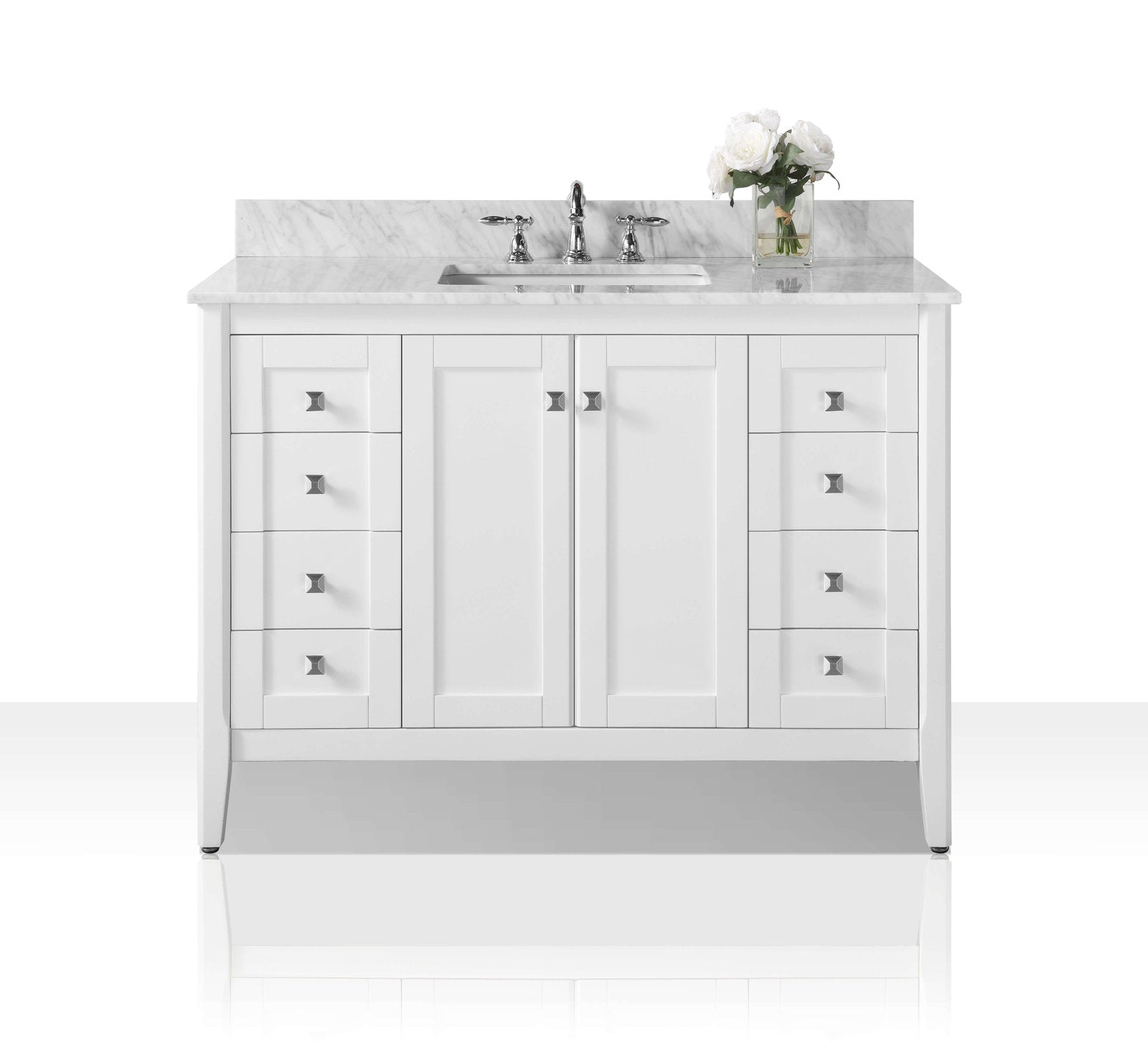 Freestanding white solid wood vanity with marble stone top and backsplash, single undermount ceramic sink and chrome faucet, shaker-style center doors flanked by stacked drawers with square chrome knobs and a vase of white flowers on top.