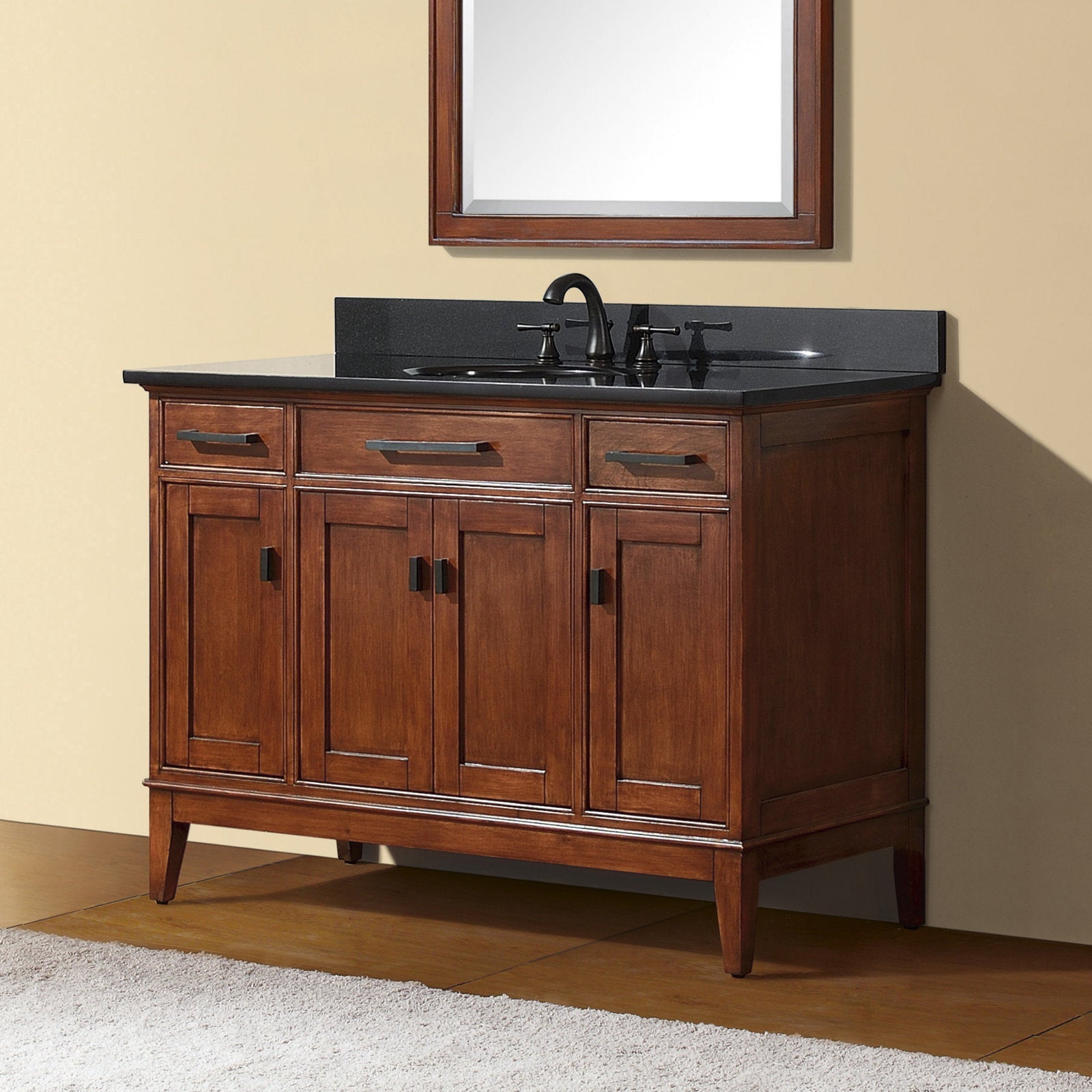 Solid wood single-sink bathroom vanity in warm brown finish with a black stone countertop and integrated ceramic sink, black faucet, three top drawers and four paneled cabinet doors, freestanding on tapered legs in a modern style.