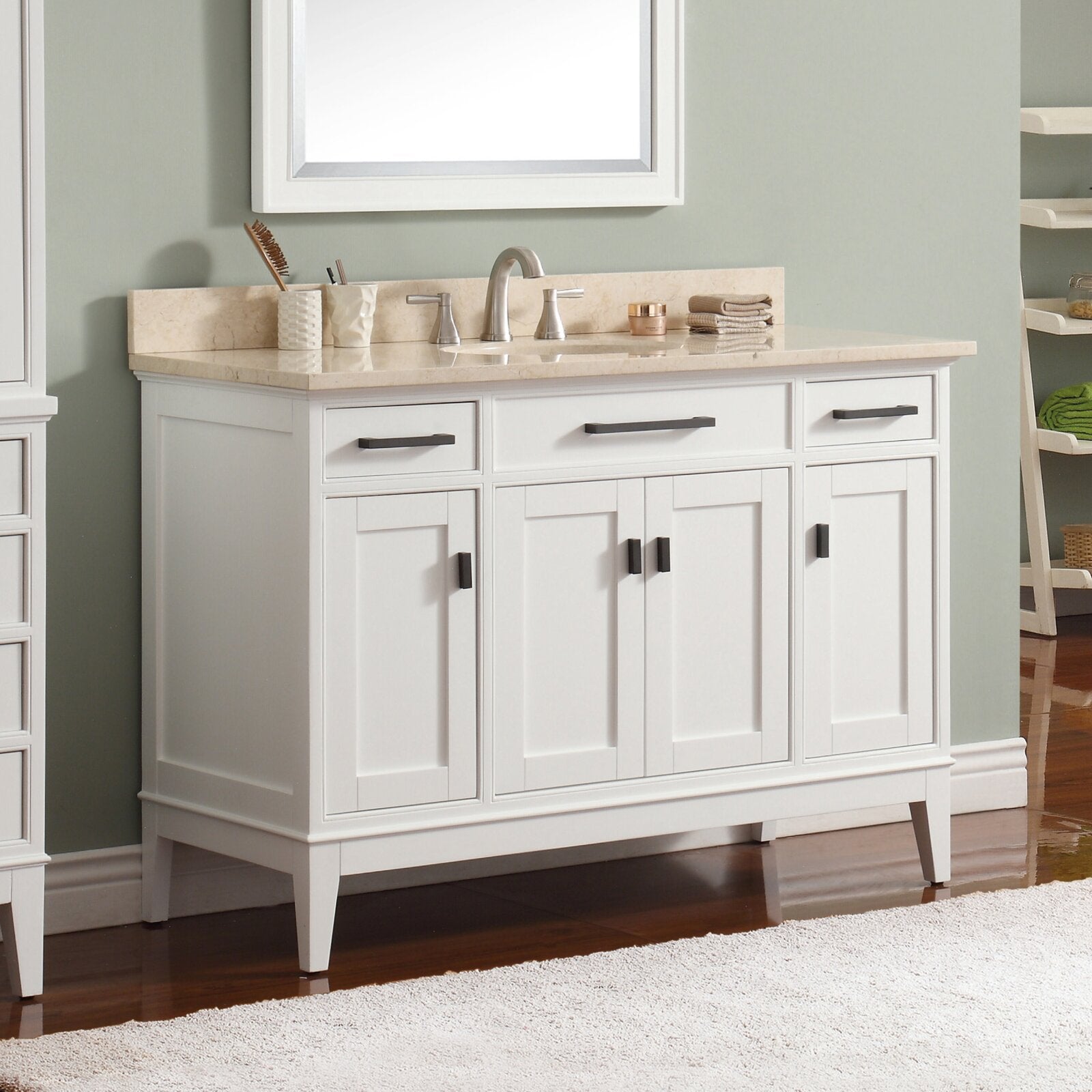 Freestanding white solid-wood bathroom vanity with a beige stone marble countertop, single ceramic sink and brushed-nickel faucet, three top drawers and paneled doors with dark rectangular handles on tapered legs.