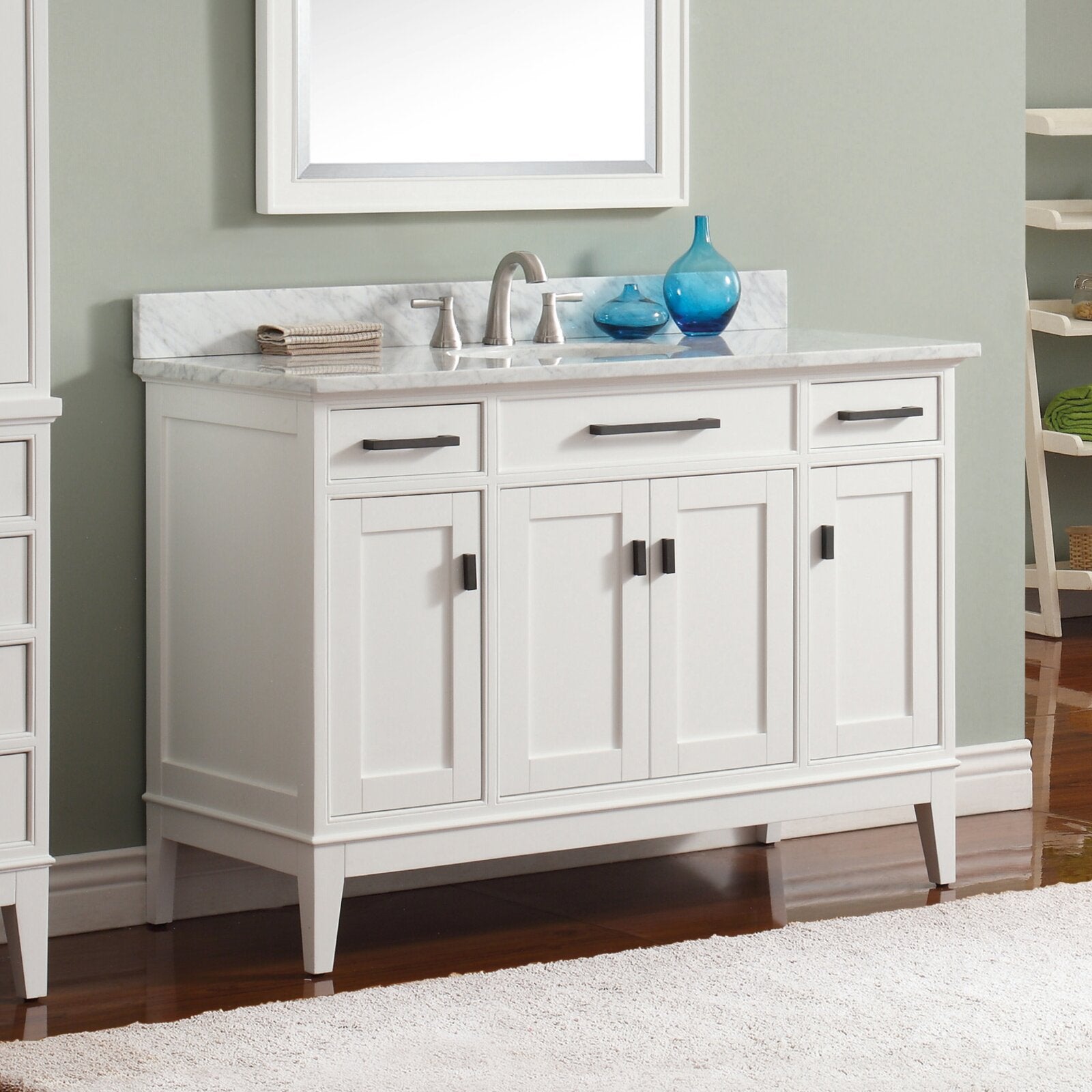 Freestanding white solid-wood single-sink bathroom vanity with marble stone countertop and backsplash, brushed nickel faucet, shaker-style doors, dark rectangular drawer and door pulls, and tapered legs on a wood floor.