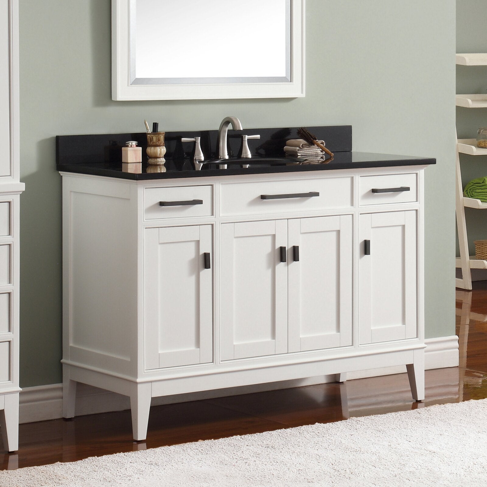 Freestanding 49-inch white solid wood bathroom vanity with black stone countertop, integrated single ceramic sink, chrome faucet, shaker-style cabinet doors and dark rectangular hardware, shown against a pale green wall.