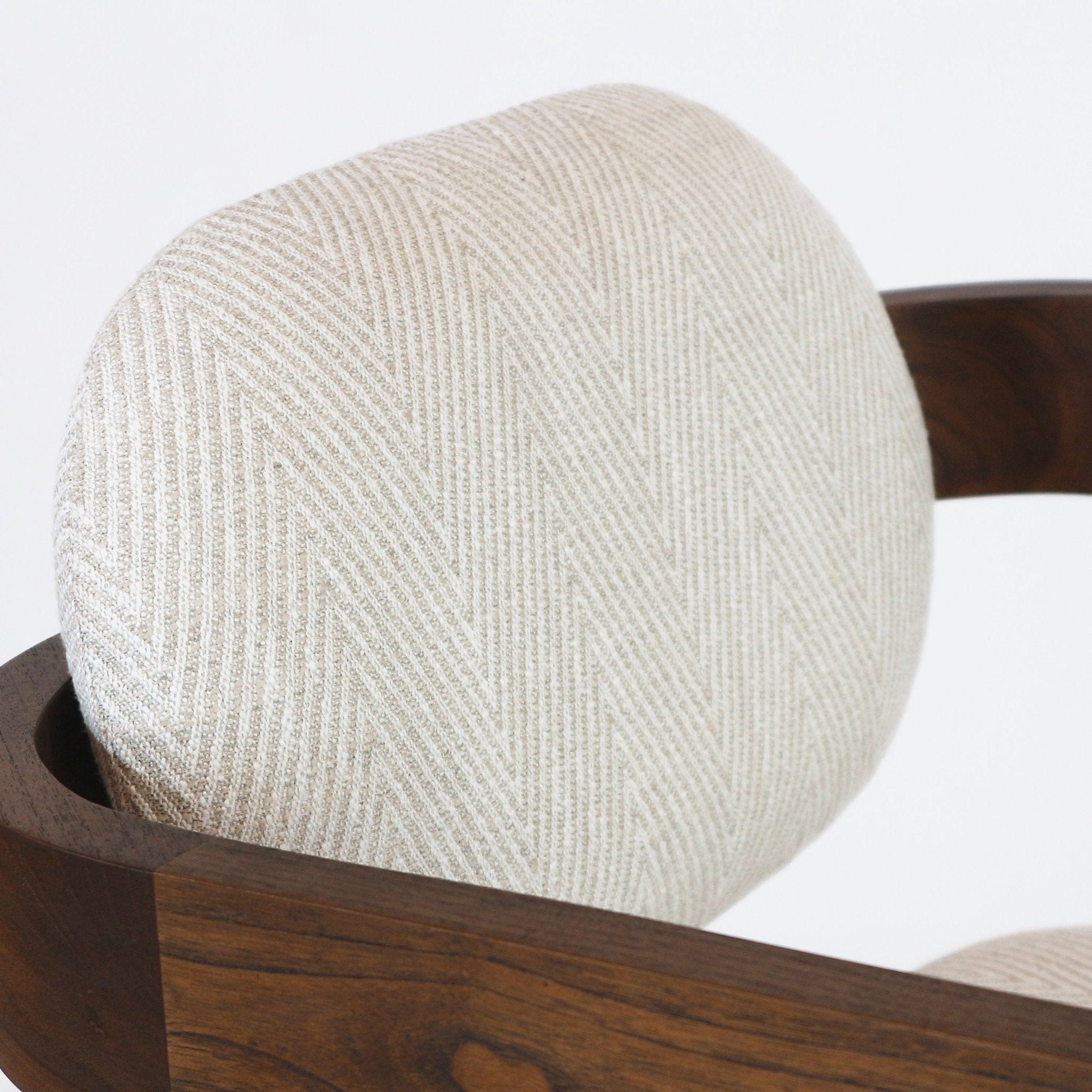 Close-up of a round bar-stool back upholstered in light beige herringbone fabric set into a curved teak natural wood frame, highlighting the textured weave and rich wood grain.