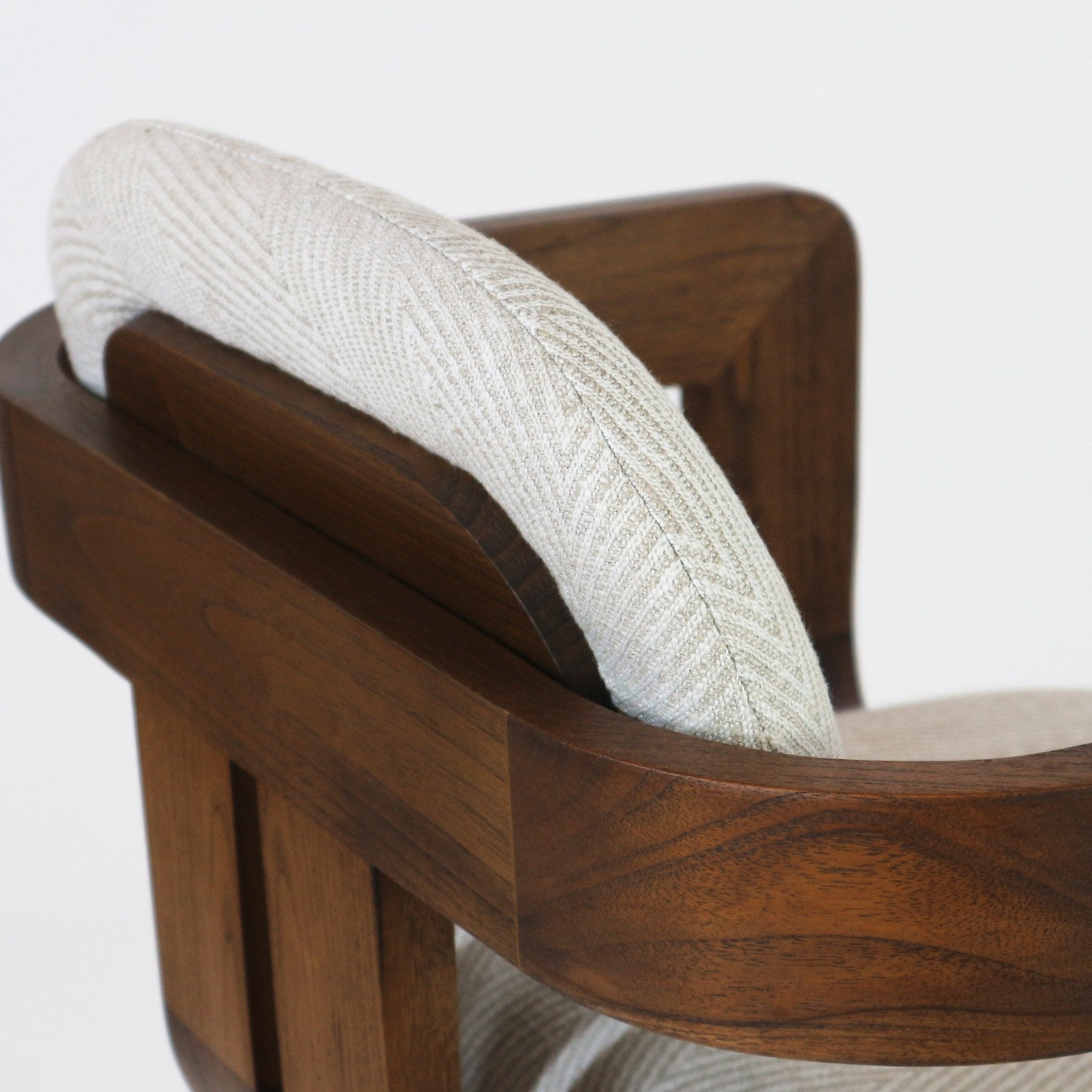Close-up of a modern bar stool showing the curved natural wood frame and padded light-gray woven fabric backrest and seat, highlighting the wood grain and textured upholstery.
