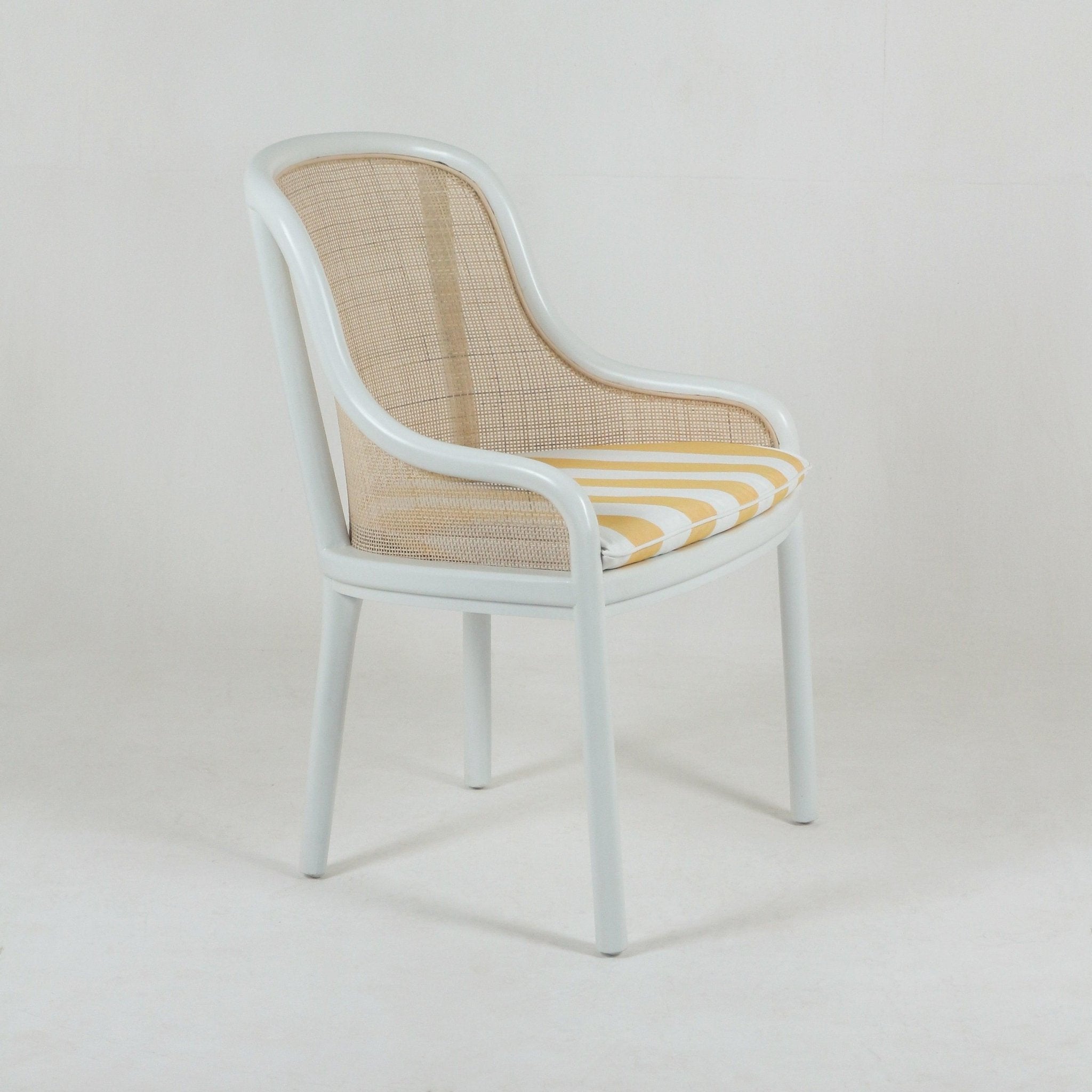White bentwood dining chair with curved arms and a natural cane back and sides, fitted with a yellow-and-white striped seat cushion on a plain light background.