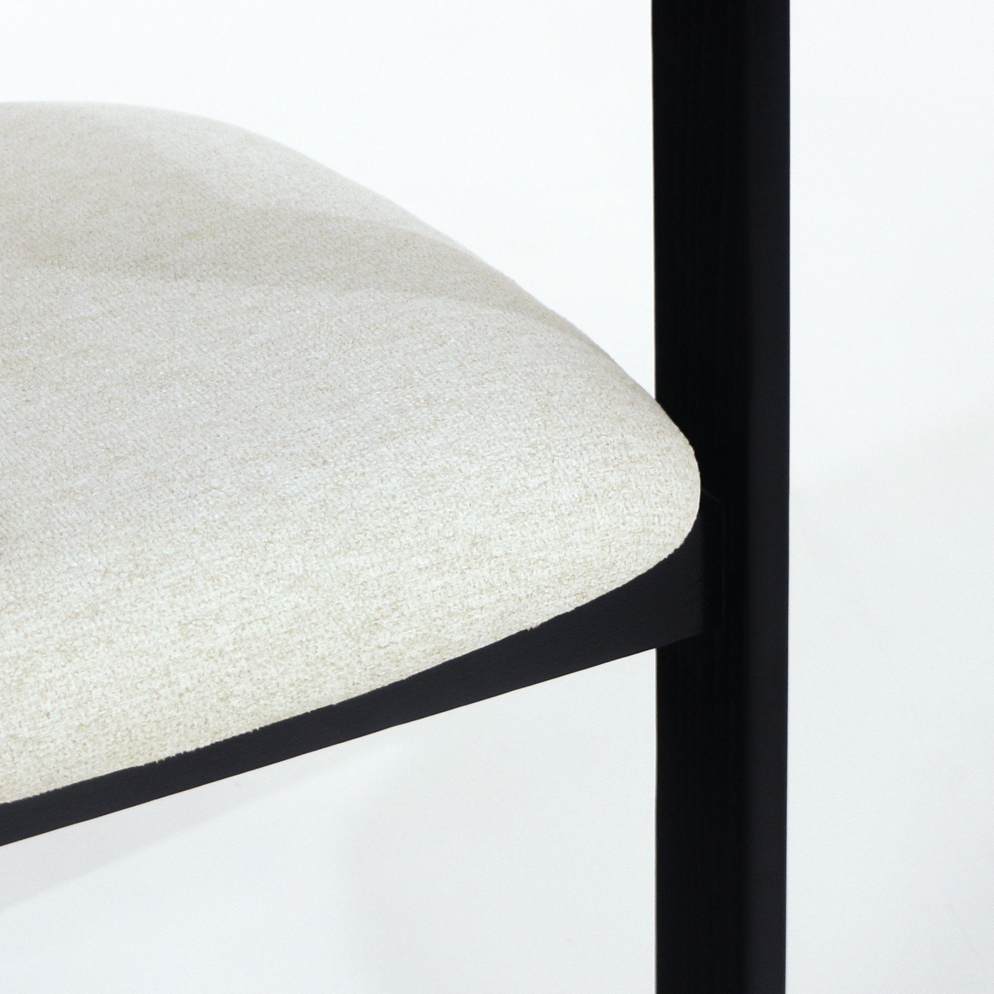 Close-up of a beige boucle upholstered dining chair seat showing the rounded cushioned edge and a slim black frame leg against a white background.