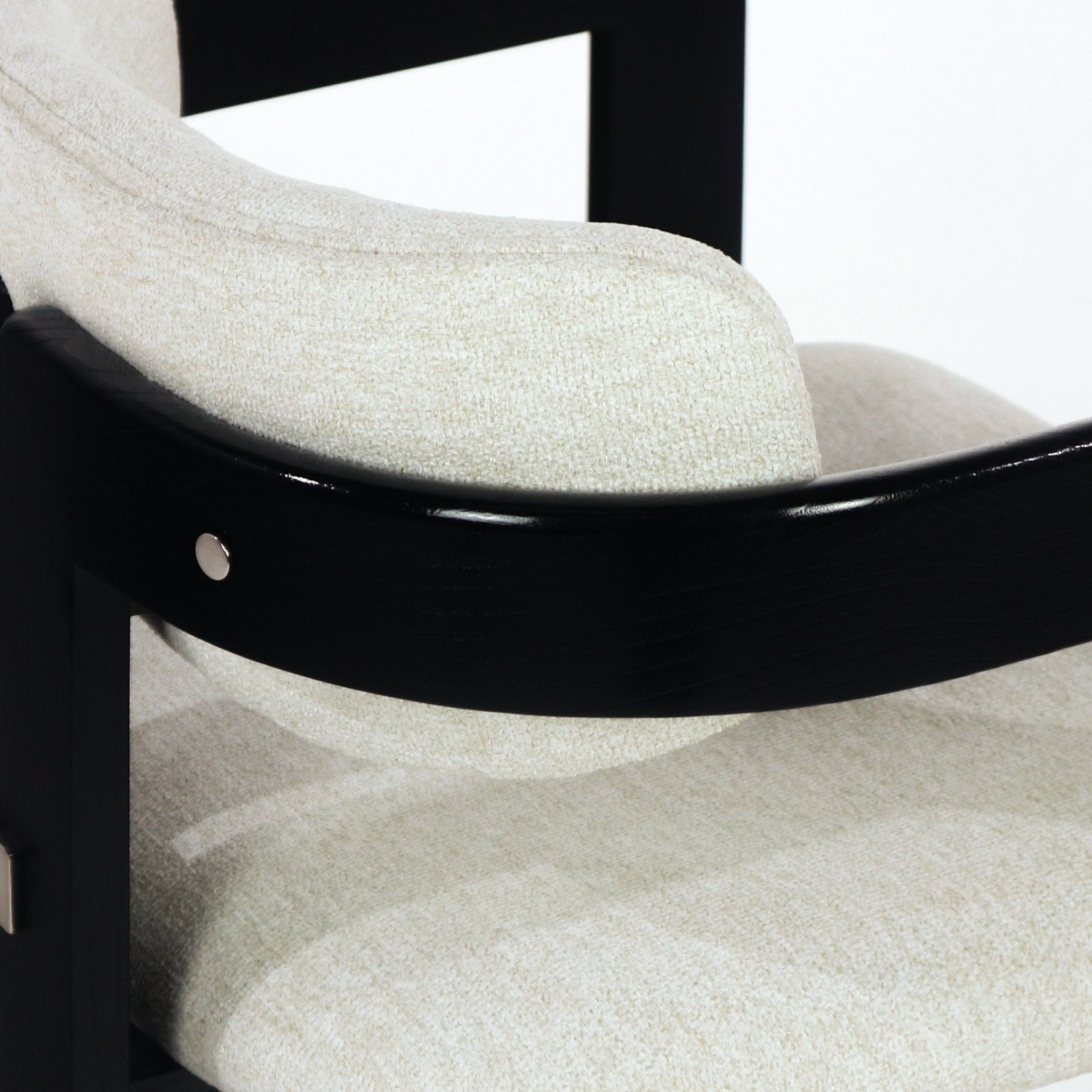 Close-up of beige boucle upholstered seat and back showing the curved black wooden frame and a round stainless-steel accent bolt.