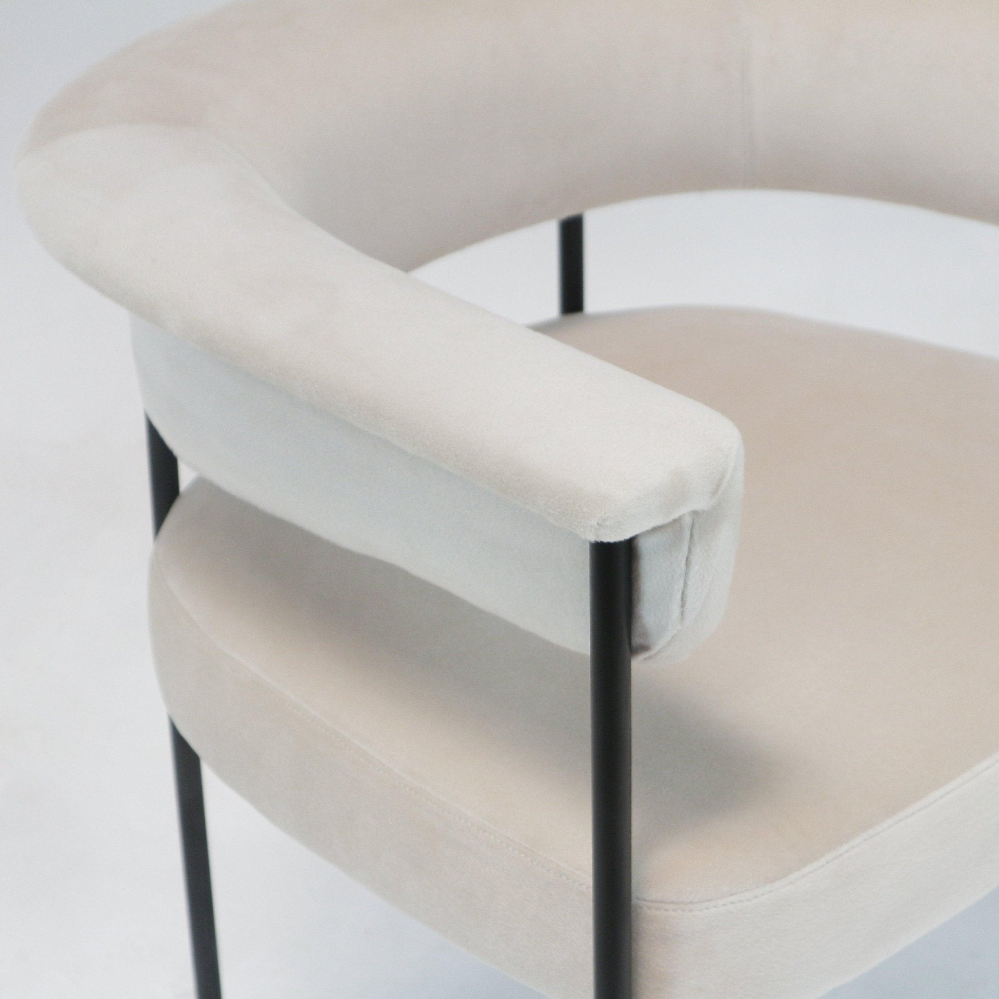 Close-up of a cream boucle upholstered dining chair showing the rounded cushioned armrest and seat supported by slender black metal legs in a modern minimalist style.