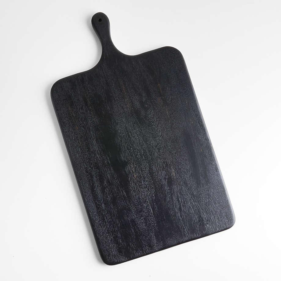 Black teak wood cutting board with rounded corners and a short handle featuring a hanging hole, showing subtle wood grain and a matte black finish on a white background.