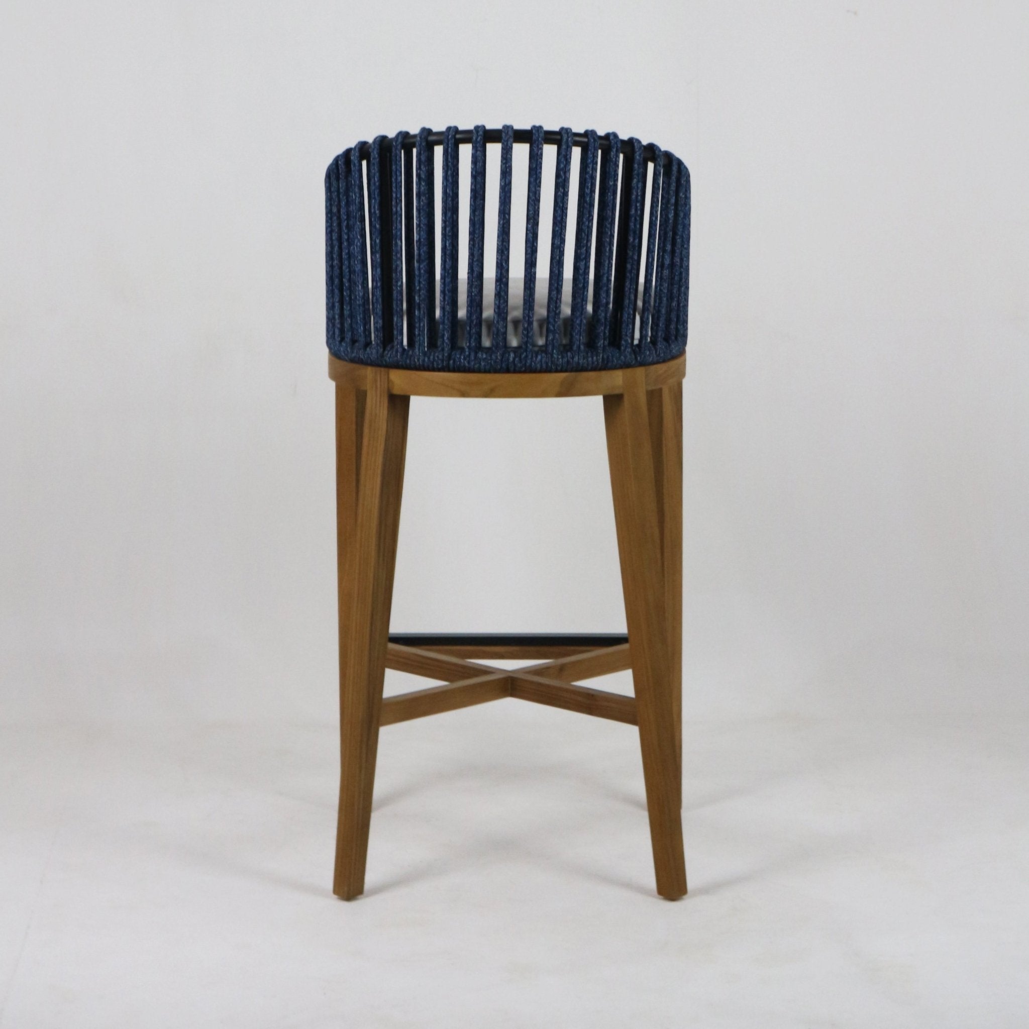 Front view of a teak outdoor bar stool with tapered wooden legs, crossed stretcher and a navy woven rope back that encircles a light gray cushioned seat.
