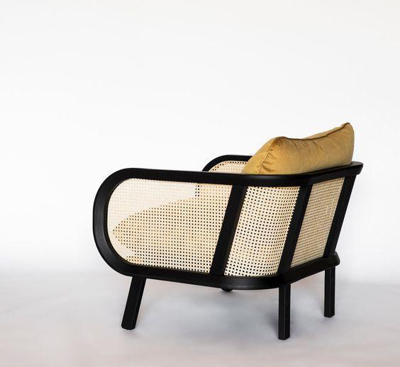 Three-quarter rear view of a modern cane armchair with a black wooden frame and woven cane panels, topped with a mustard-yellow fabric seat cushion on a plain white background.