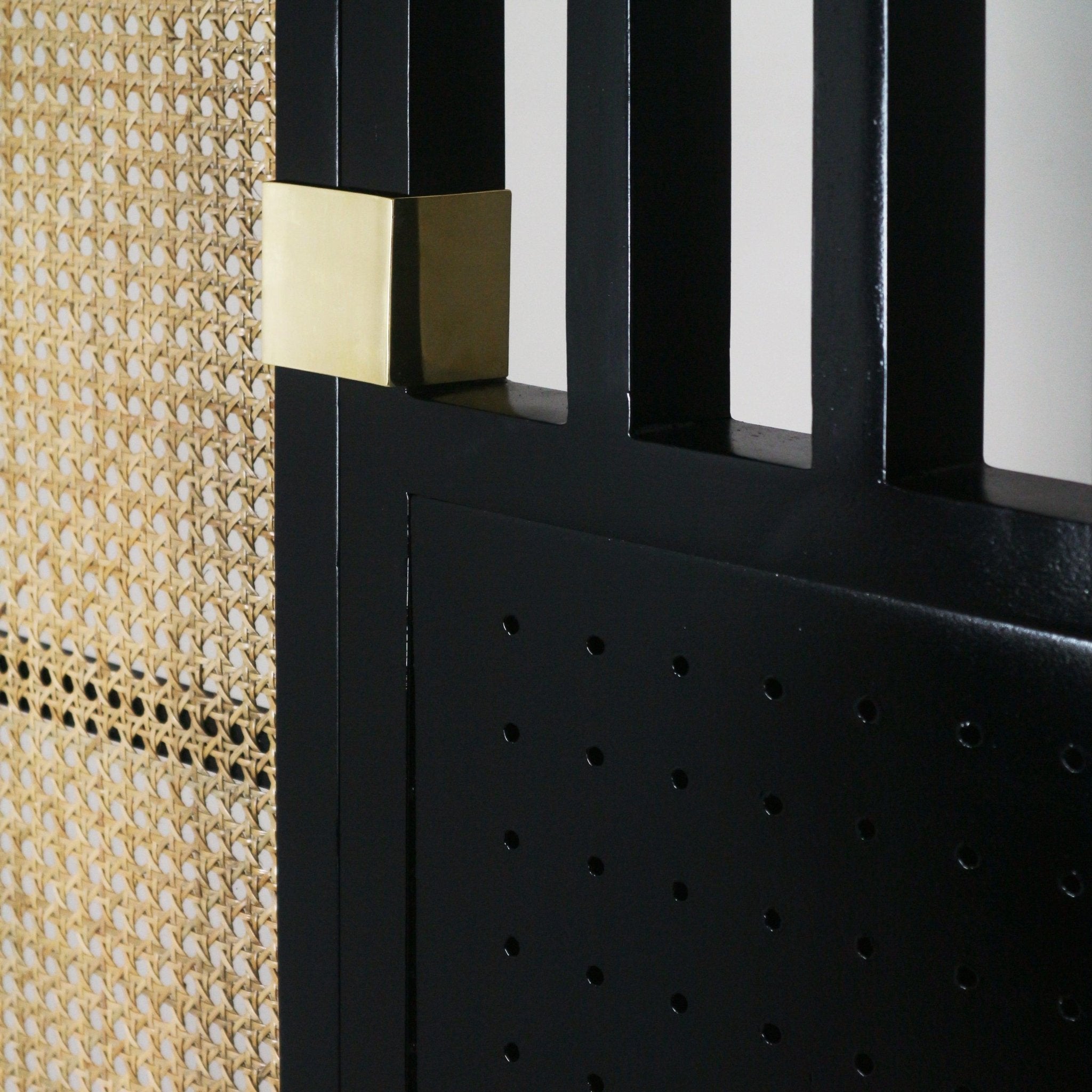 Close-up of an oak headboard detail showing a black metal frame with a brass rectangular cap beside a natural rattan cane weave panel.
