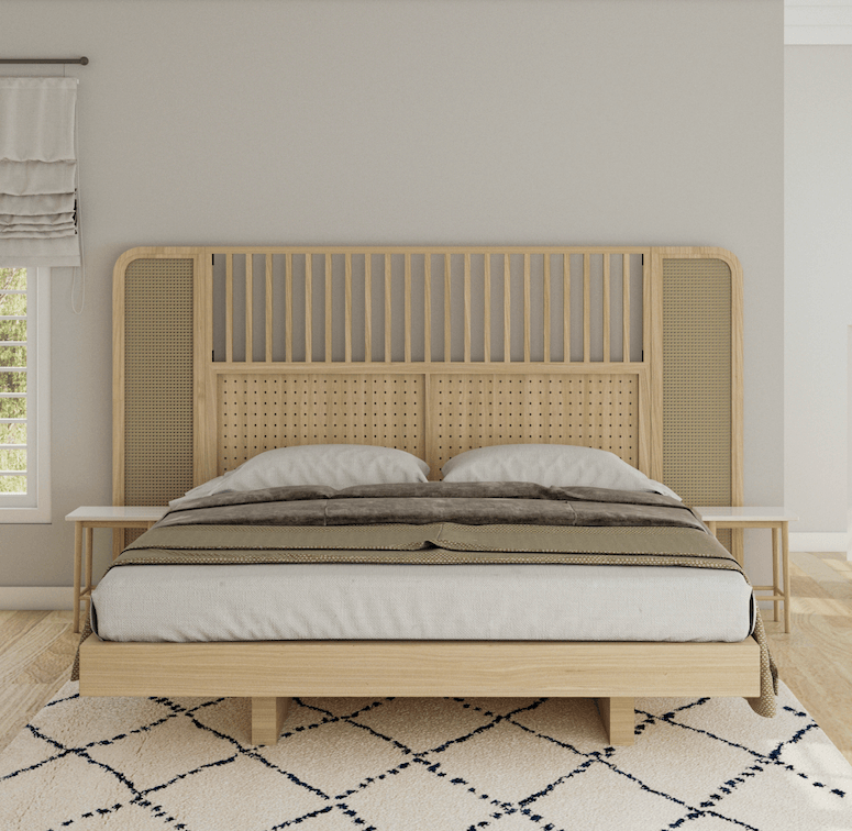 Oak rattan headboard with vertical slats and woven cane side panels behind a low oak platform bed with neutral linens, white nightstands, and a cream patterned rug in a light boho-style bedroom.
