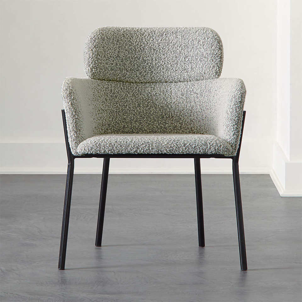 Front-facing grey boucle upholstered dining chair with curved backrest, integrated low arms and a padded headrest detail, set on slim black metal legs against a neutral floor and wall.