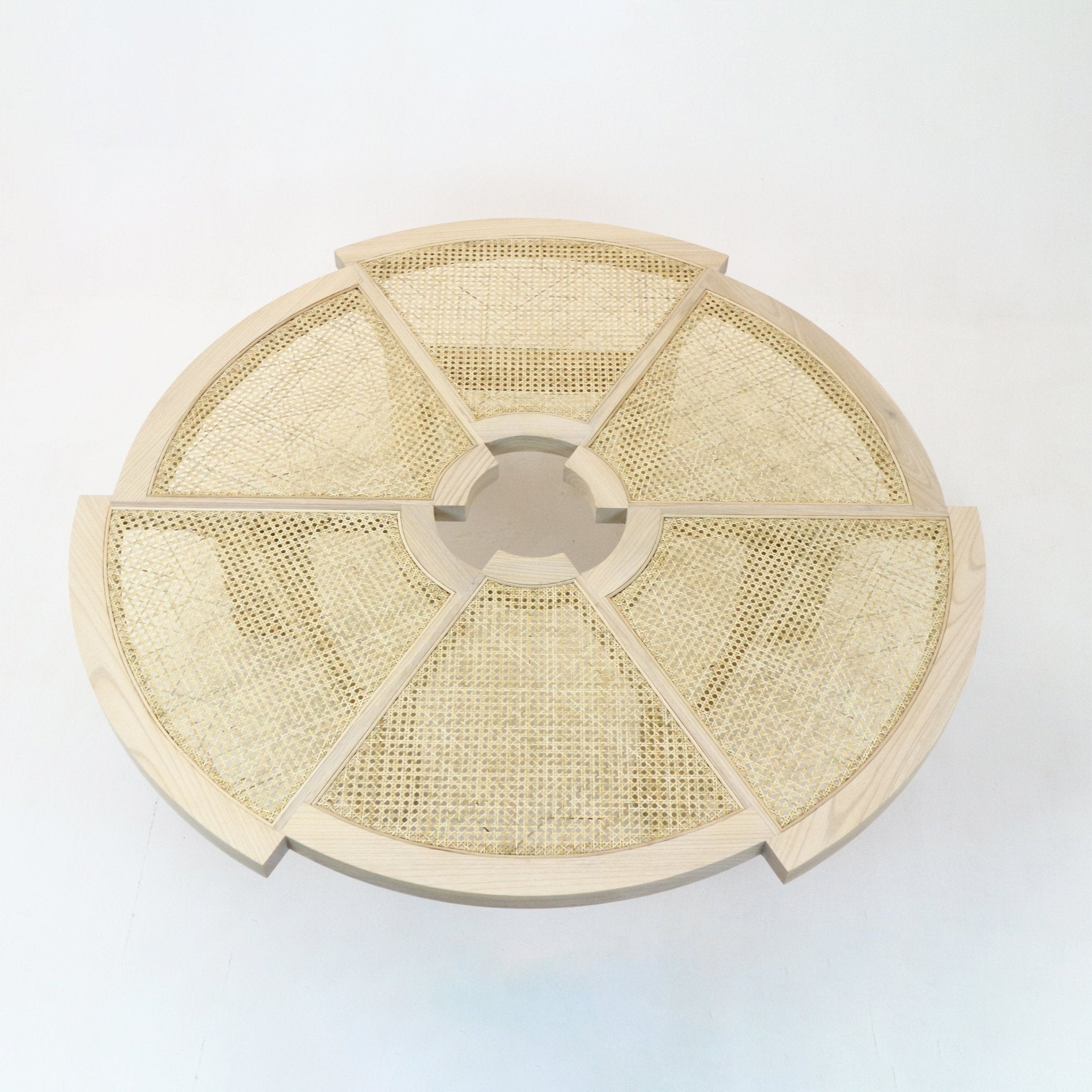 Top-down view of a round coffee table in natural blonde oak with six cane-woven wedge panels radiating from a central circular opening, showing a modern minimalist solid wood frame and woven rattan surface.