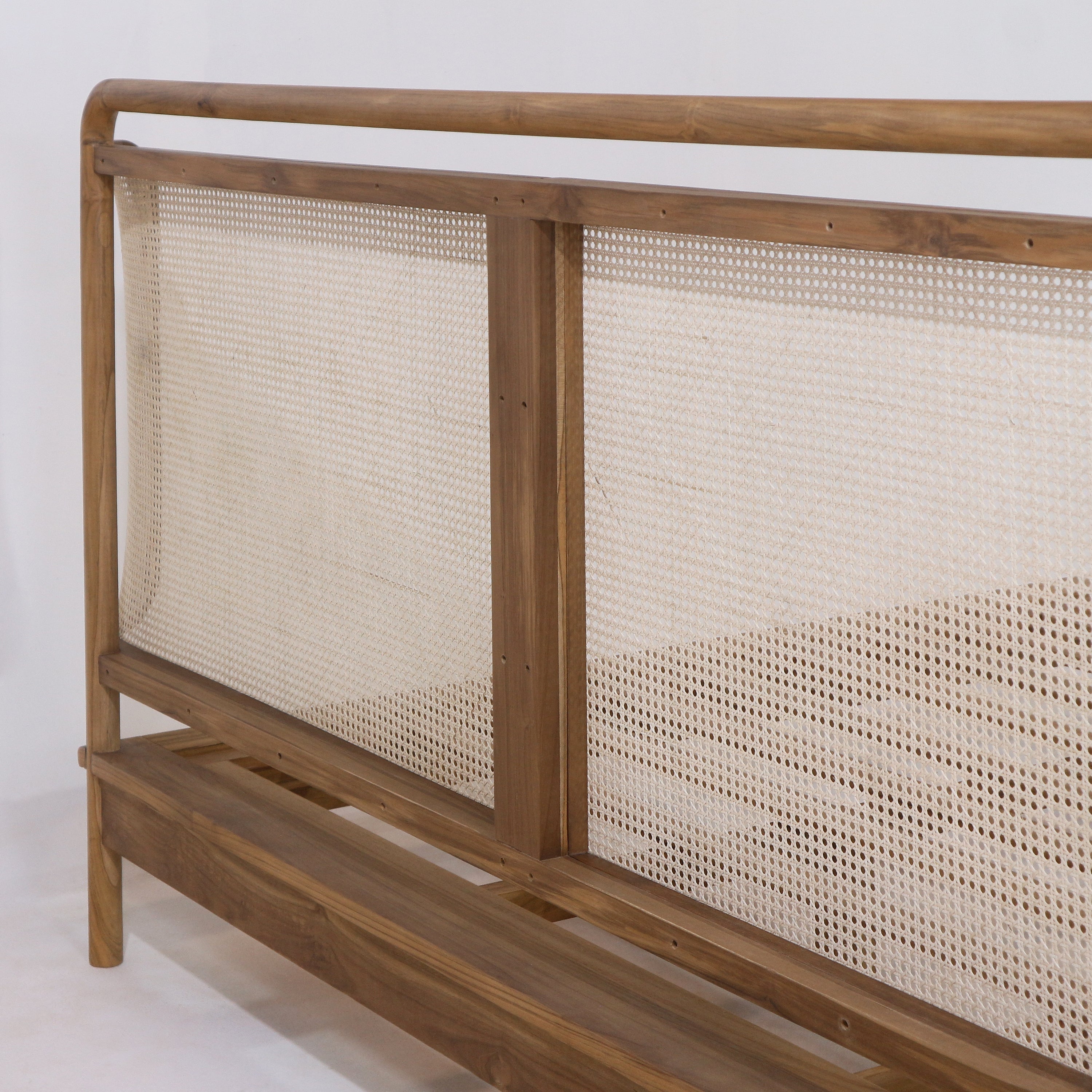 Close-up of a teak bed headboard showing a natural teak frame with a woven rattan cane panel and visible platform base in a boho style finish.