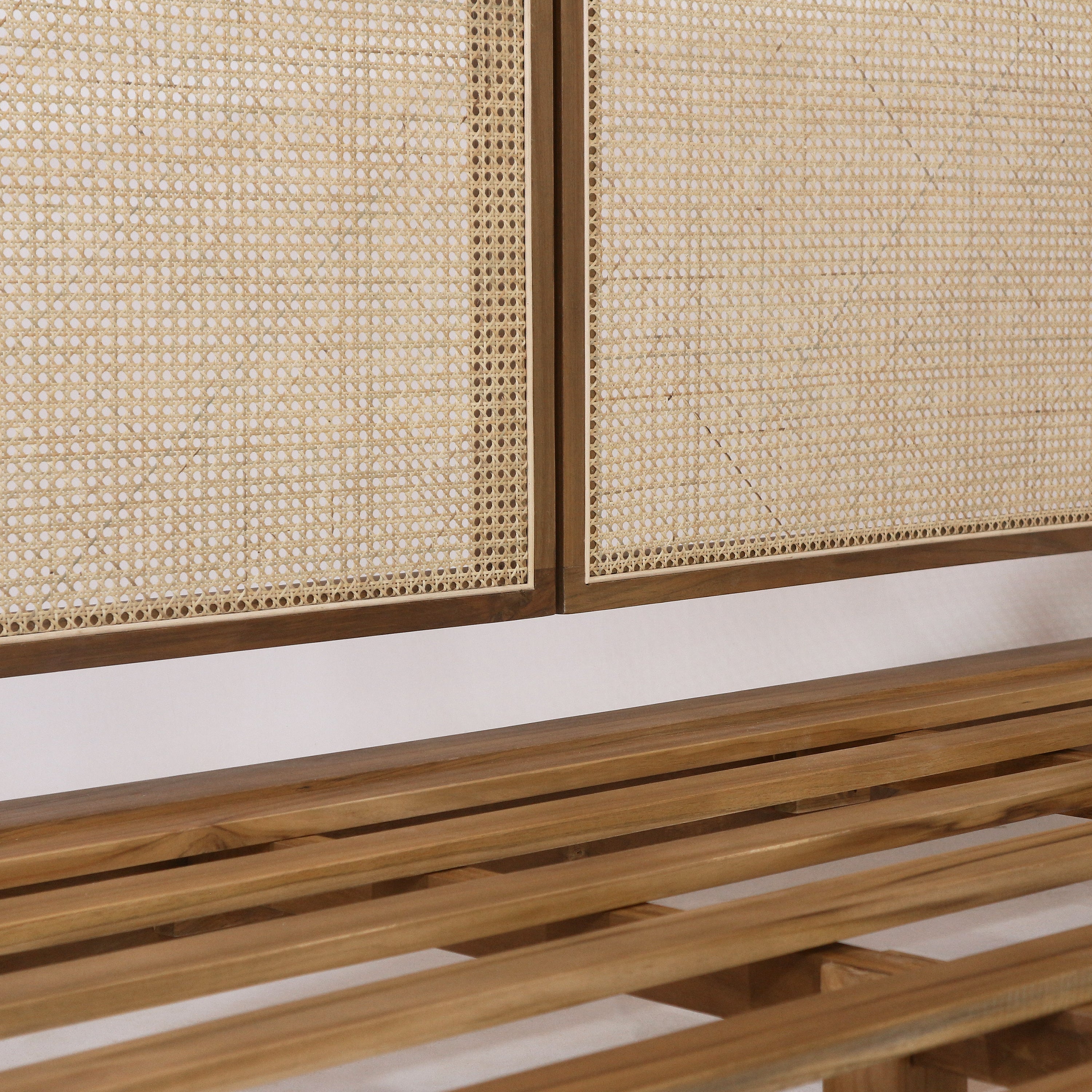 Close-up of a boho-style teak bed showing natural rattan cane-weave headboard panels framed in teak and a matching slatted teak bed base.