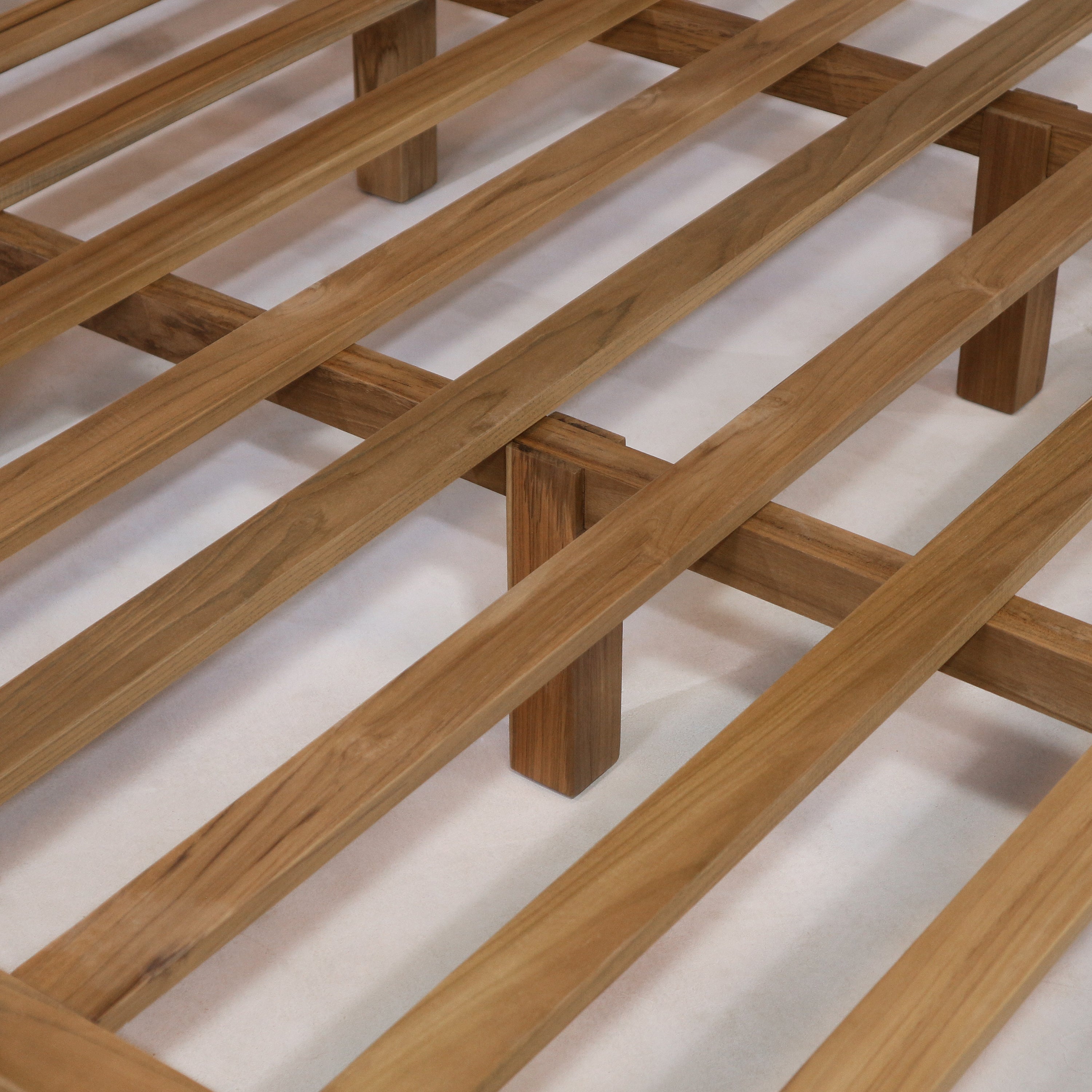 Close-up of a teak slatted bed base showing natural teak wood slats and a central support leg, highlighting the smooth grain and slat spacing for a boho-style platform bed.