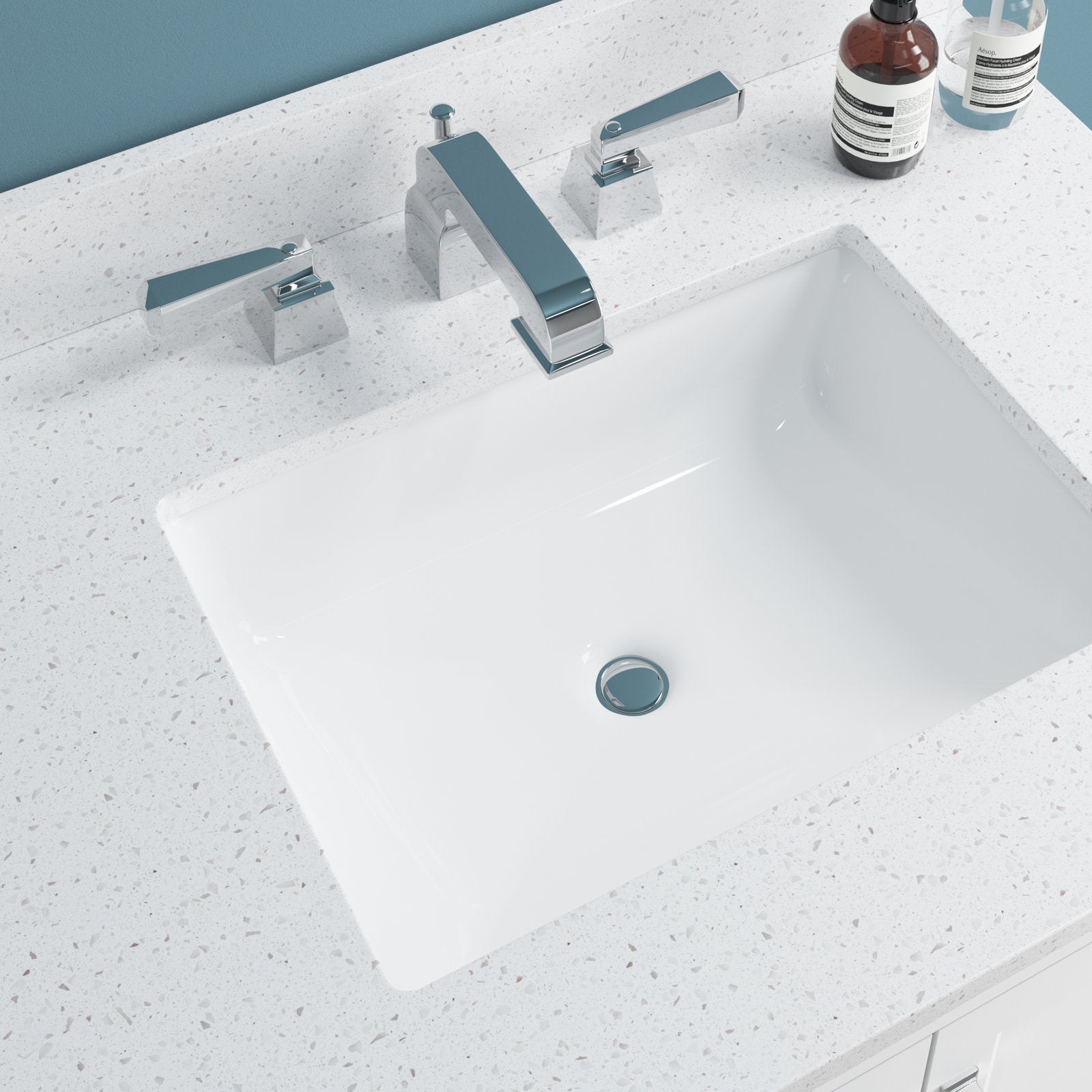 Overhead view of a white rectangular ceramic sink set in a speckled stone countertop with a chrome widespread faucet and two soap bottles on a modern 31-inch single-sink bathroom vanity.