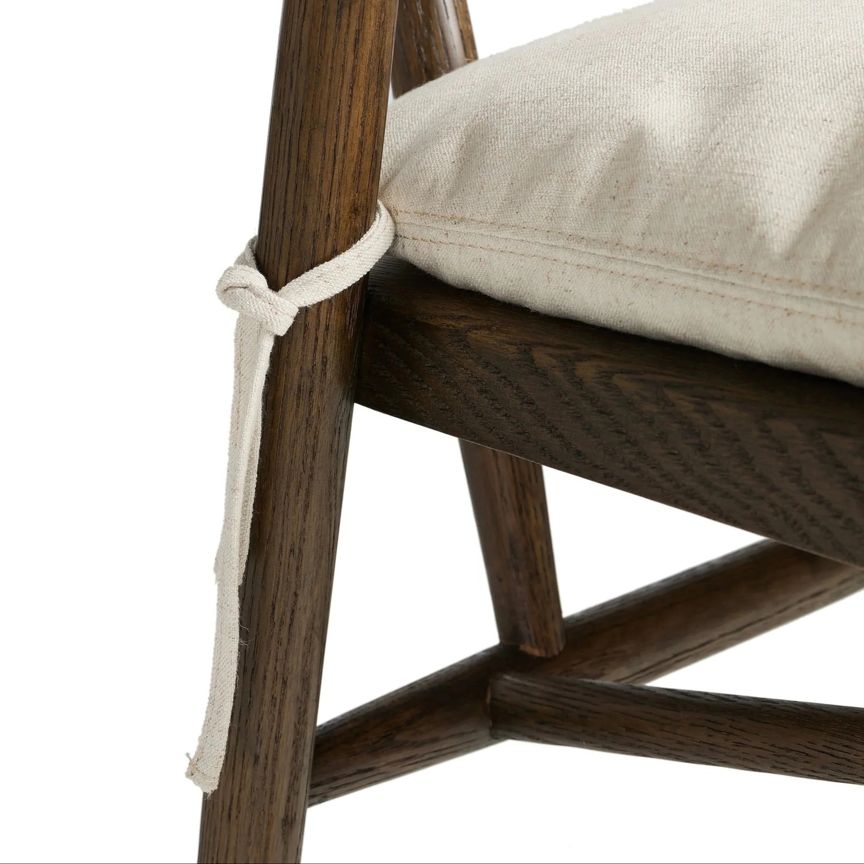 Close-up of a natural wood stool frame showing a cream-colored fabric cushion secured with a tied rope-style fabric strap around the leg, highlighting wood grain and the cushion's stitched seam.