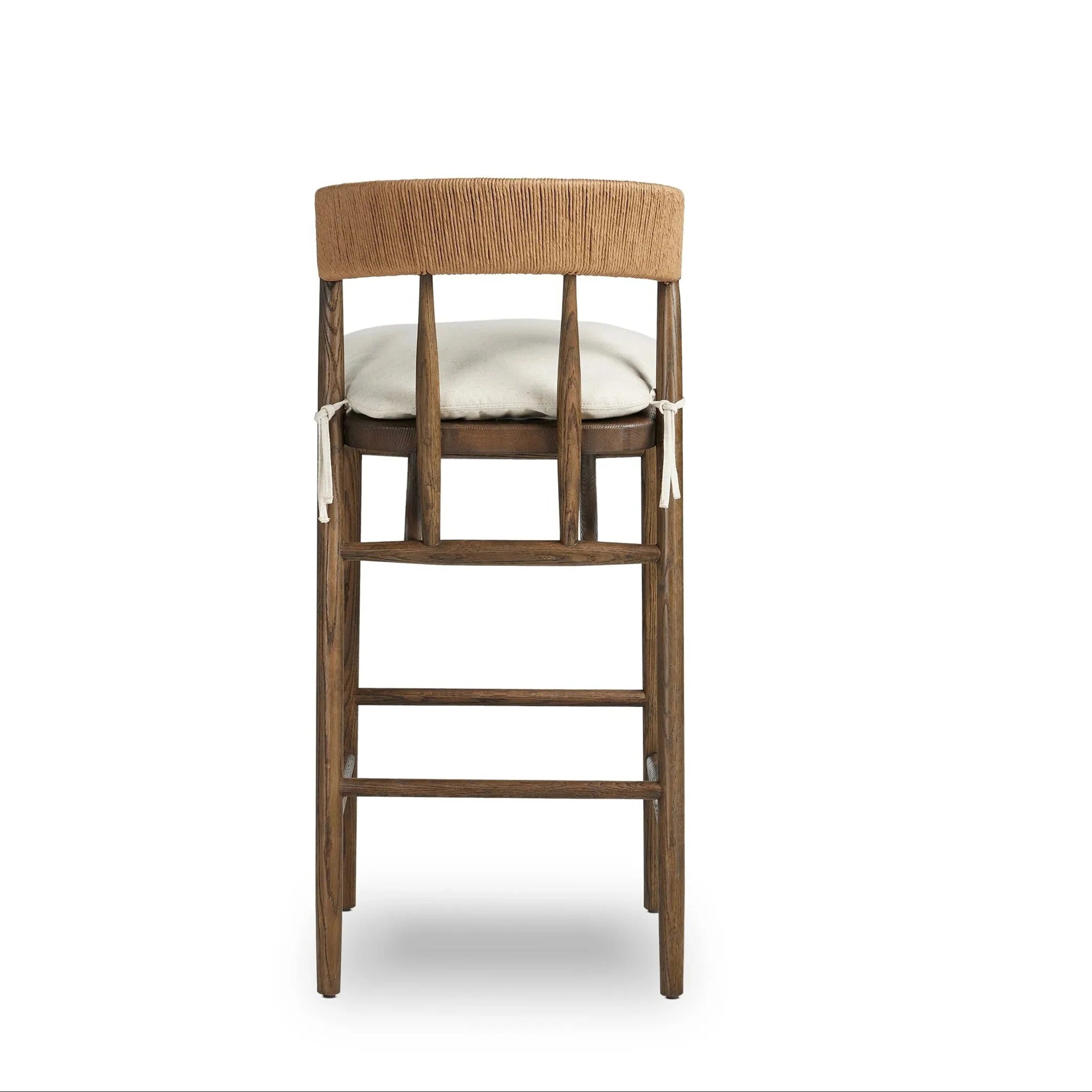 Rear view of a rustic natural wood bar stool with a tan rope-wrapped C-shaped back, off-white cushioned seat secured with fabric ties, and a sturdy wood frame with horizontal footrest rungs.