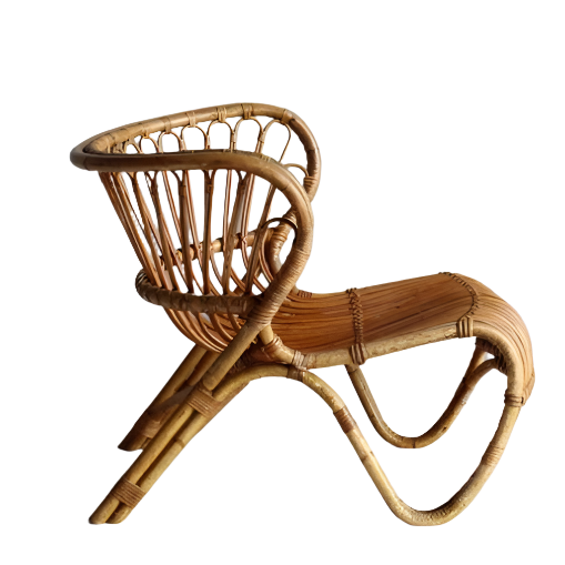 Natural rattan armless lounge chair with a curved woven frame, open slatted back, low contoured seat and looping bent-rattan legs in a boho-Scandinavian style.