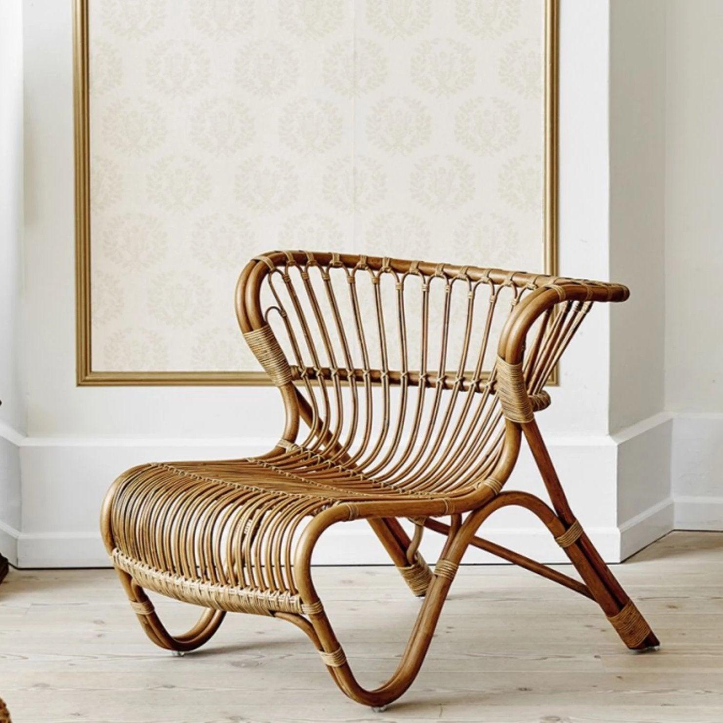 Natural rattan armless lounge chair with curved woven slat seat and back in a boho-Scandinavian style, displayed in a bright room on light wood flooring.