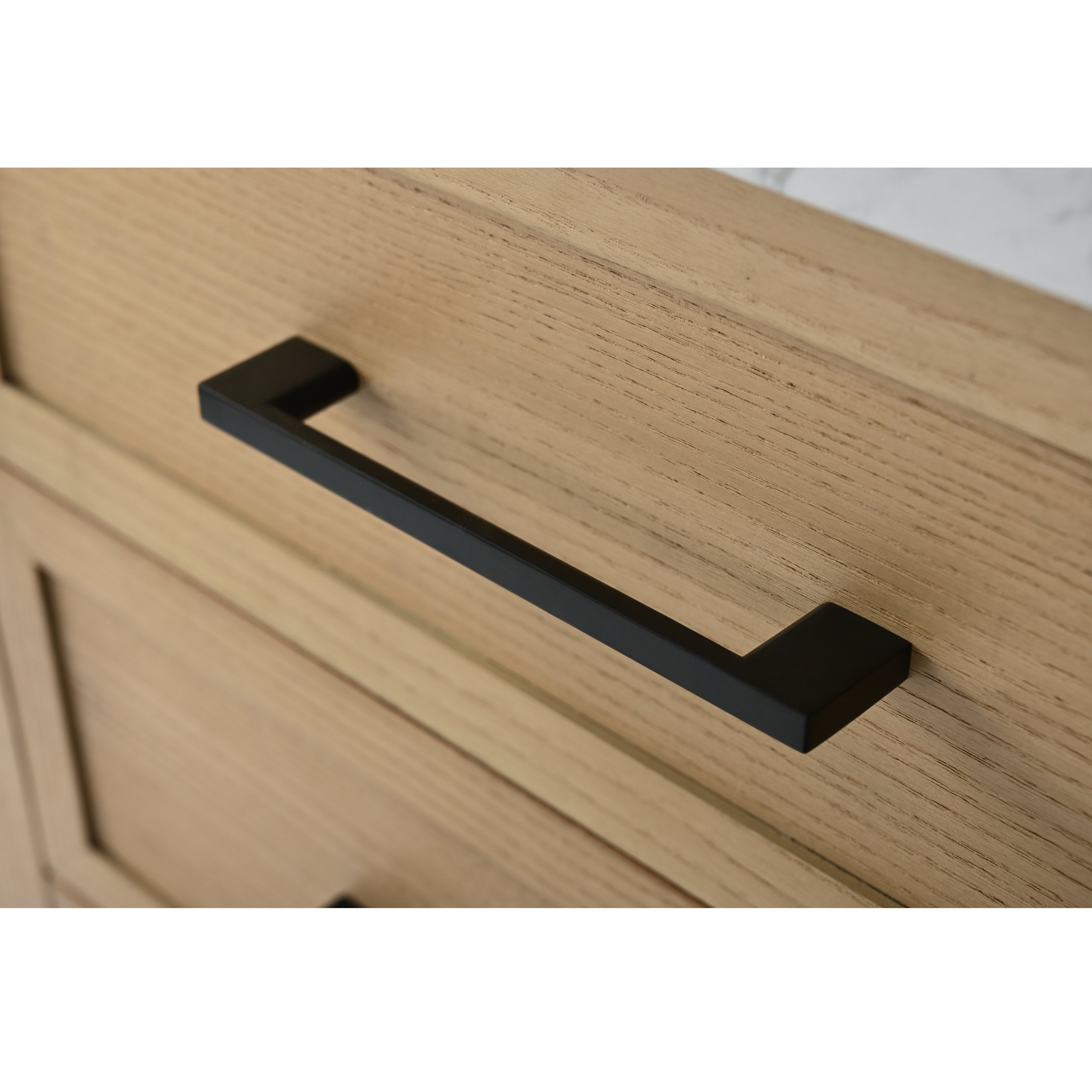 Close-up of a matte black bar drawer handle mounted on a light stone-colored solid wood vanity drawer front, highlighting the wood grain and modern rectangular pull.