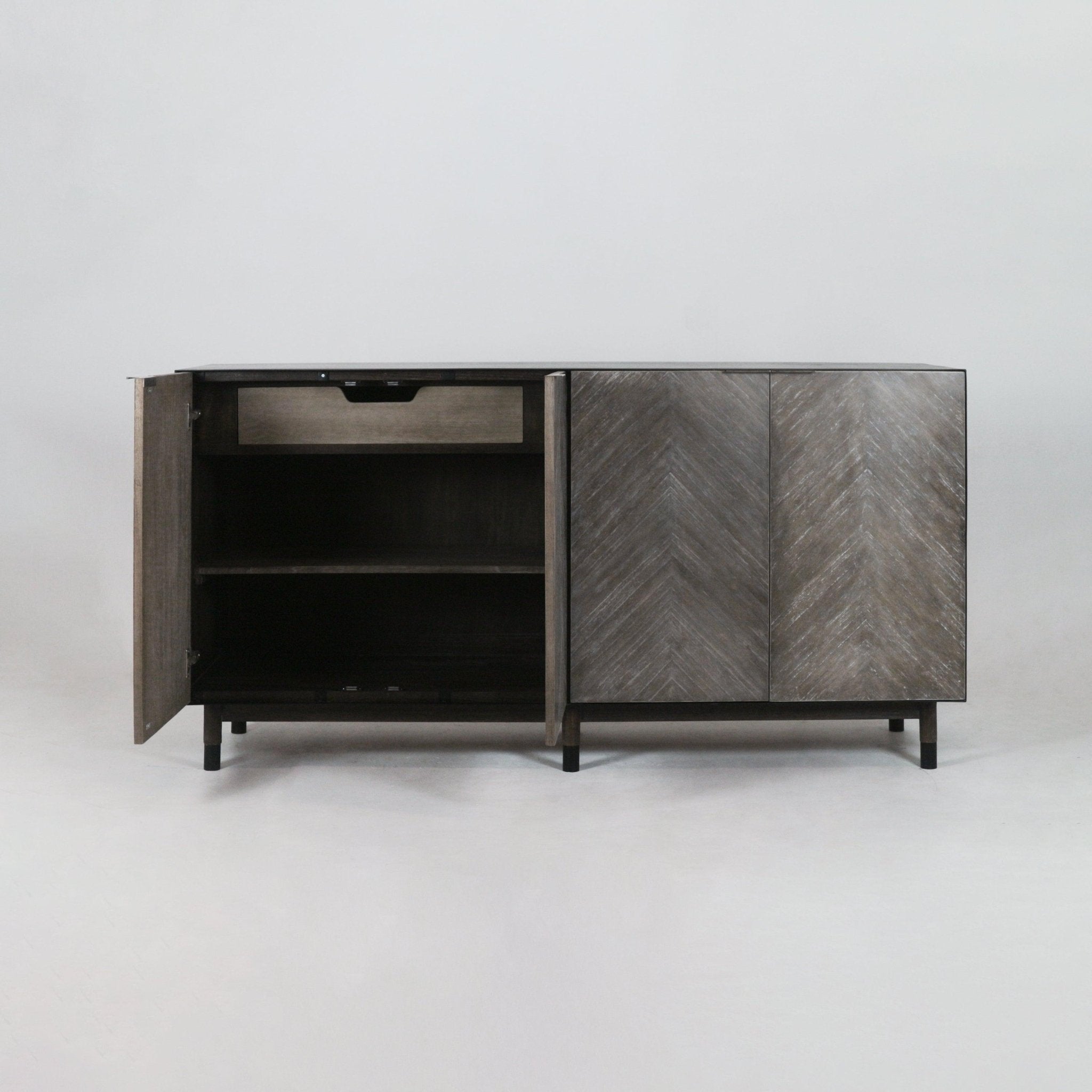 Mid-century modern teak sideboard with gray-brown chevron-pattern doors; left door open to reveal an interior drawer and two shelves, raised on slender black metal legs.
