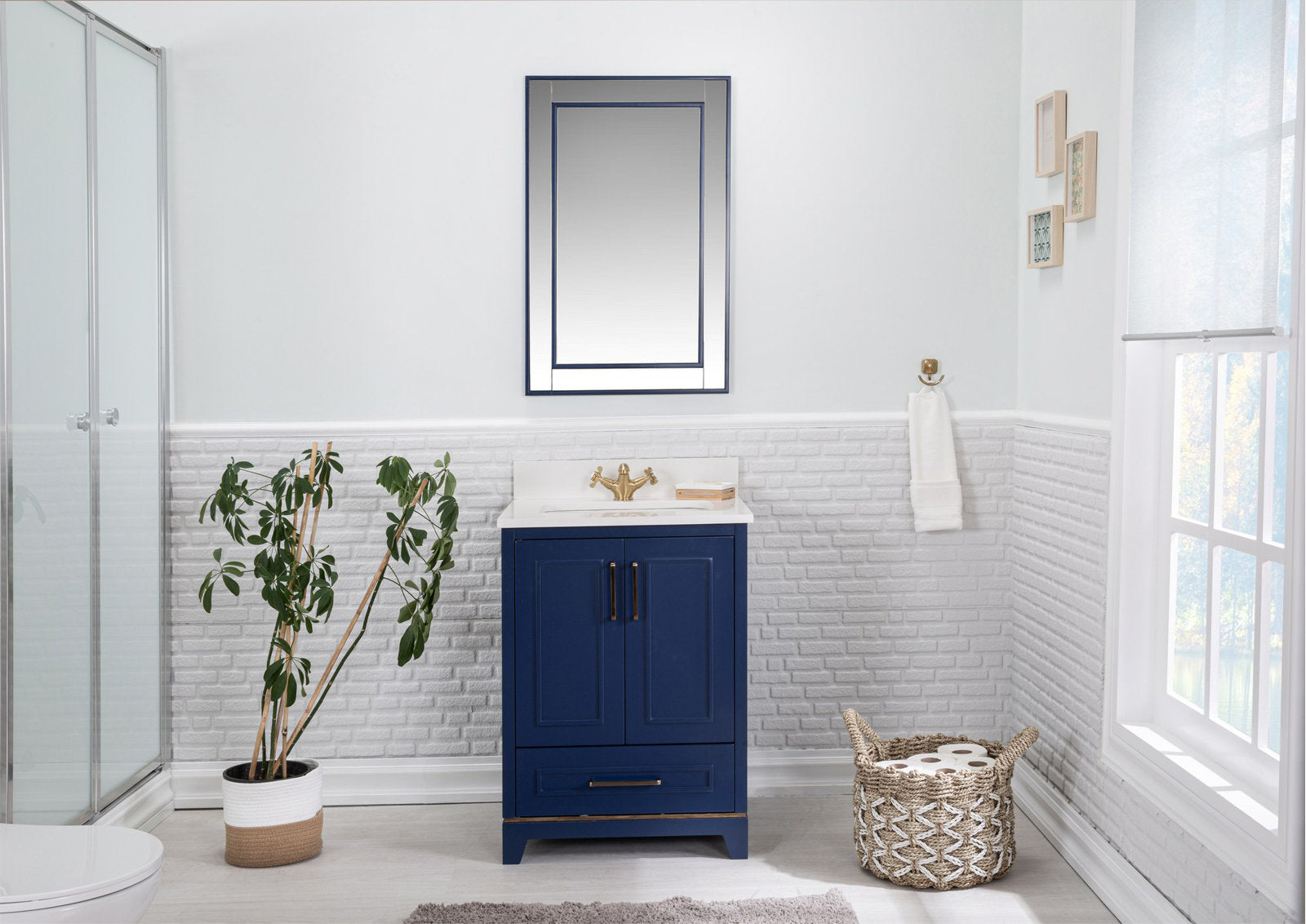 Modern solid wood single-sink bathroom vanity with a stone countertop, navy-blue freestanding cabinet, brass hardware and white sink, shown with matching mirror, potted plant and woven basket in a bright bathroom.