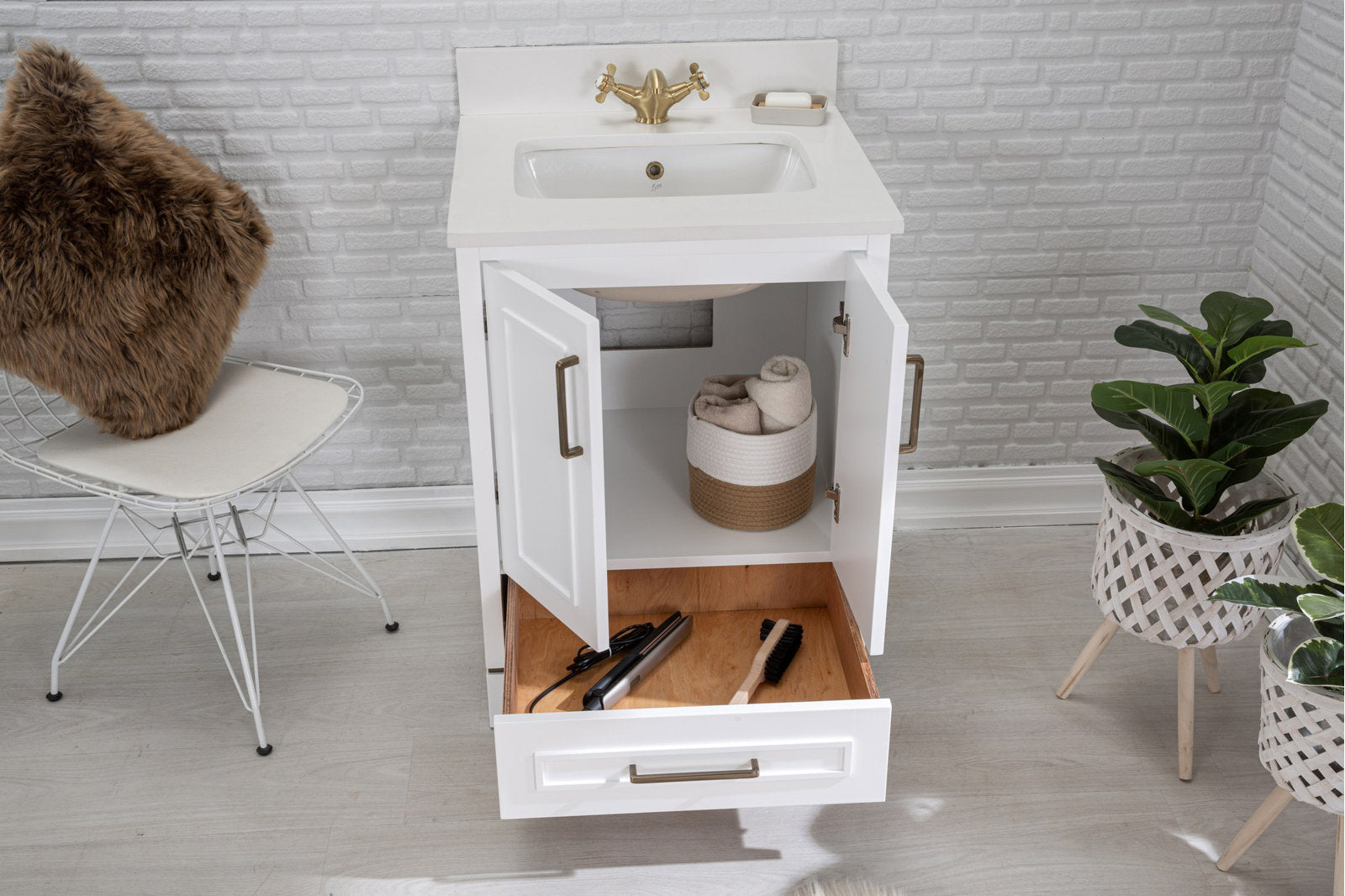 White modern solid wood bathroom vanity with stone top and undermount ceramic sink, brass faucet; open doors reveal woven basket with rolled towels and the lower drawer holds a hair straightener and brush.
