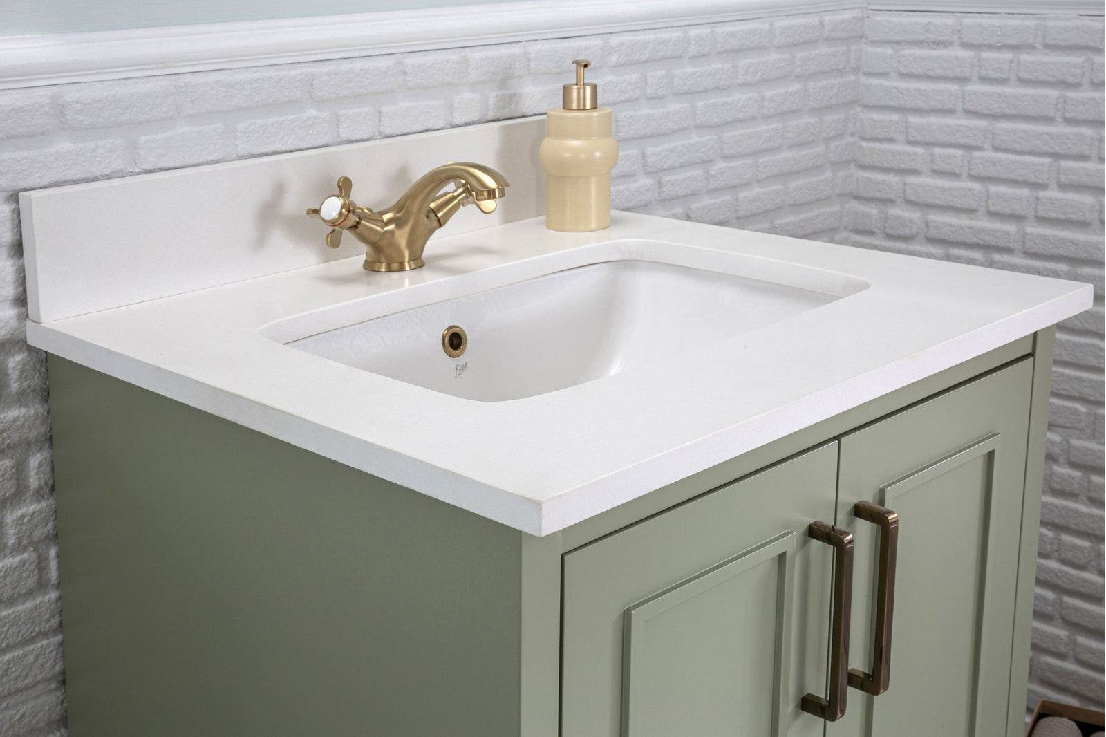 Modern solid wood bathroom vanity with a white stone countertop and integrated ceramic sink, olive-green painted cabinet, brass faucet and matching rectangular brass handles, shown against a white textured brick backsplash with a beige soap dispenser