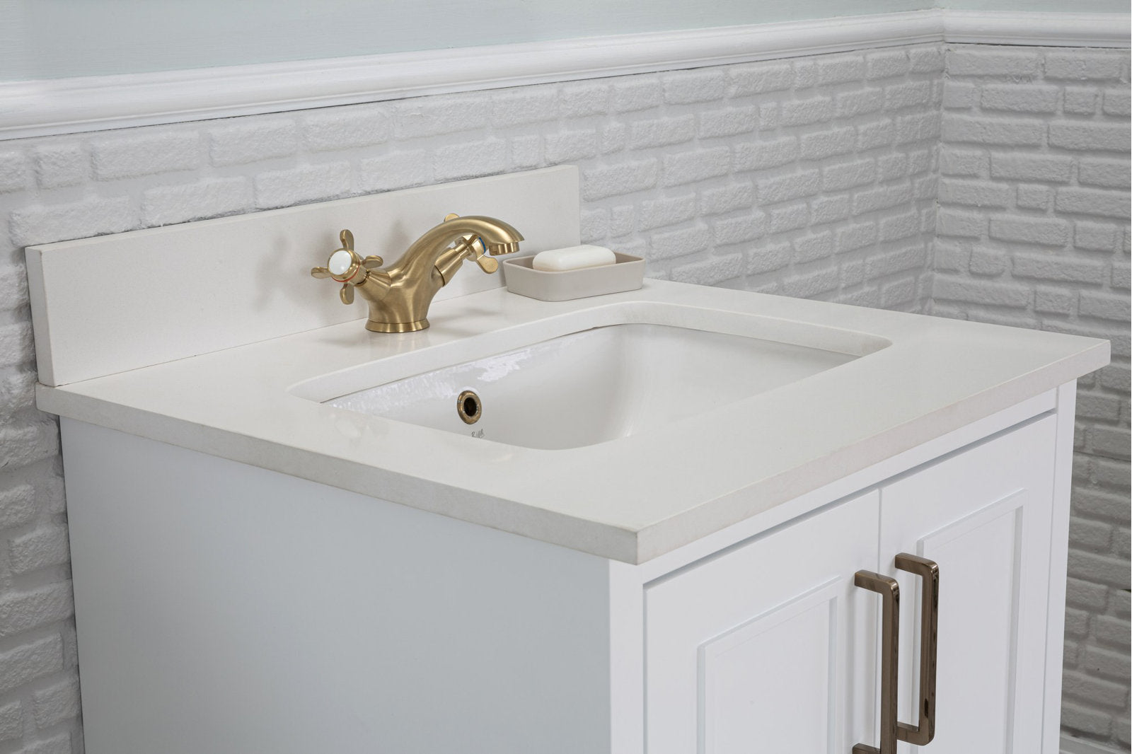 Modern solid wood bathroom vanity with a stone top and integrated white ceramic sink, paired with a brass two-handle faucet, small soap dish, and white paneled cabinet with bronze handles.
