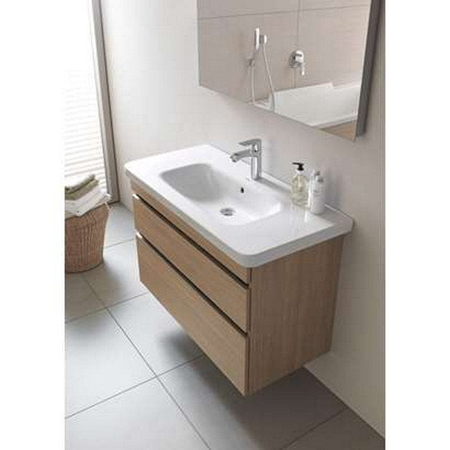 Wall-mounted modern bathroom vanity in natural solid wood with a stone-colored integrated ceramic single sink top, chrome faucet and two horizontal drawers, shown beneath a mirror on light grey tiled floor.