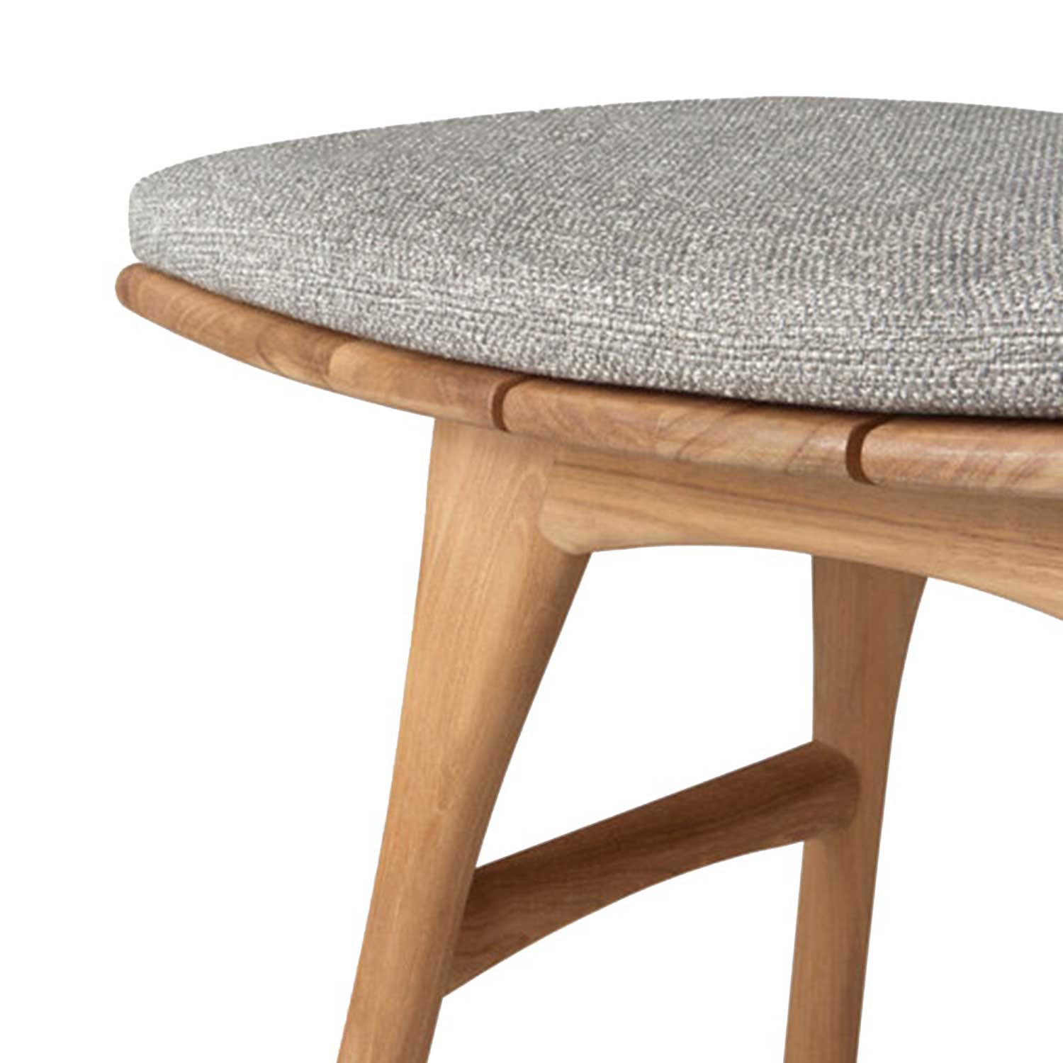 Close-up of a light gray upholstered seat cushion on a natural teak shower stool, showing the rounded teak seat rail, tapered leg and curved stretcher in a coastal-inspired solid wood frame.